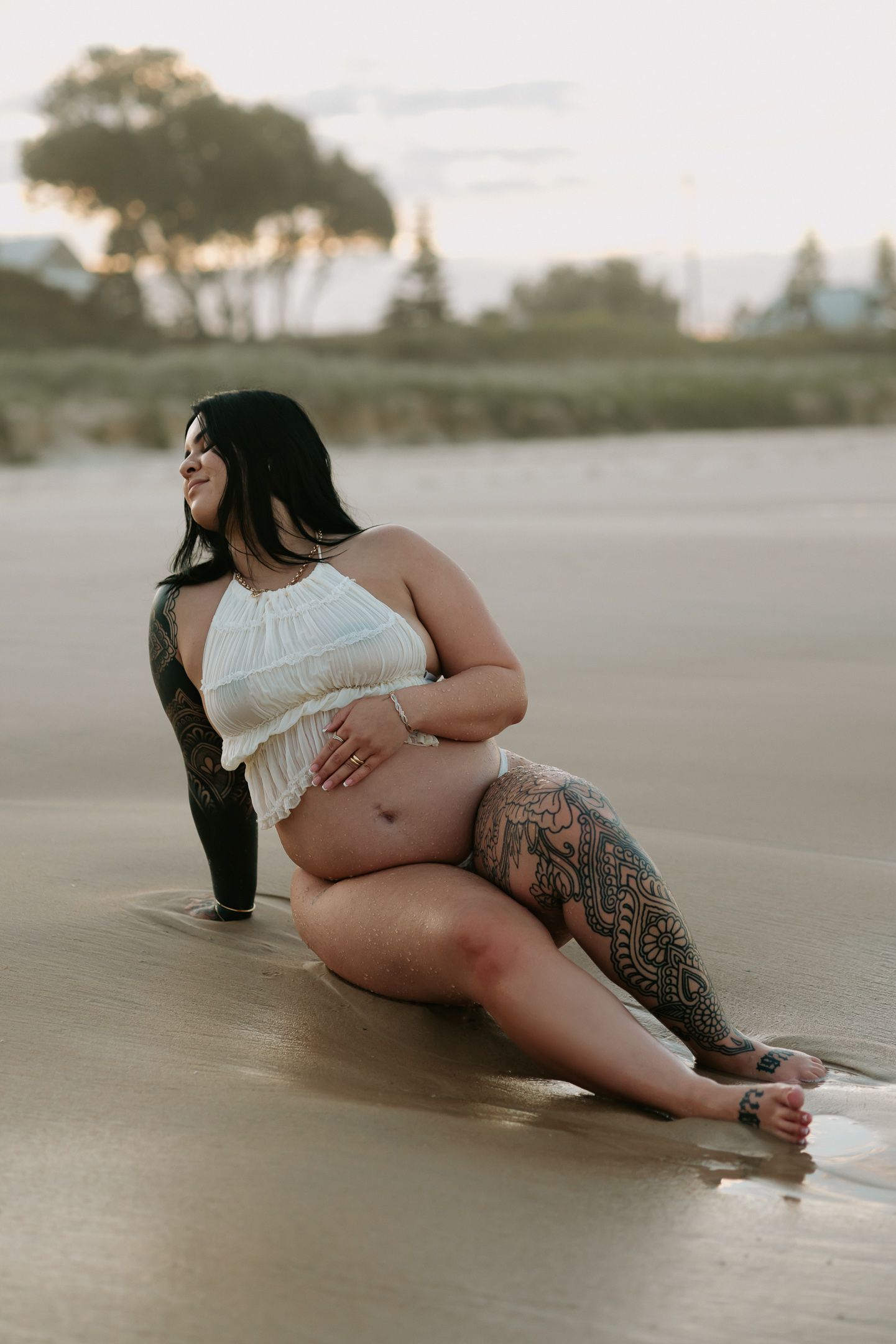 Artistic boudoir photo series showing figure reclining on sandy beach at sunset.