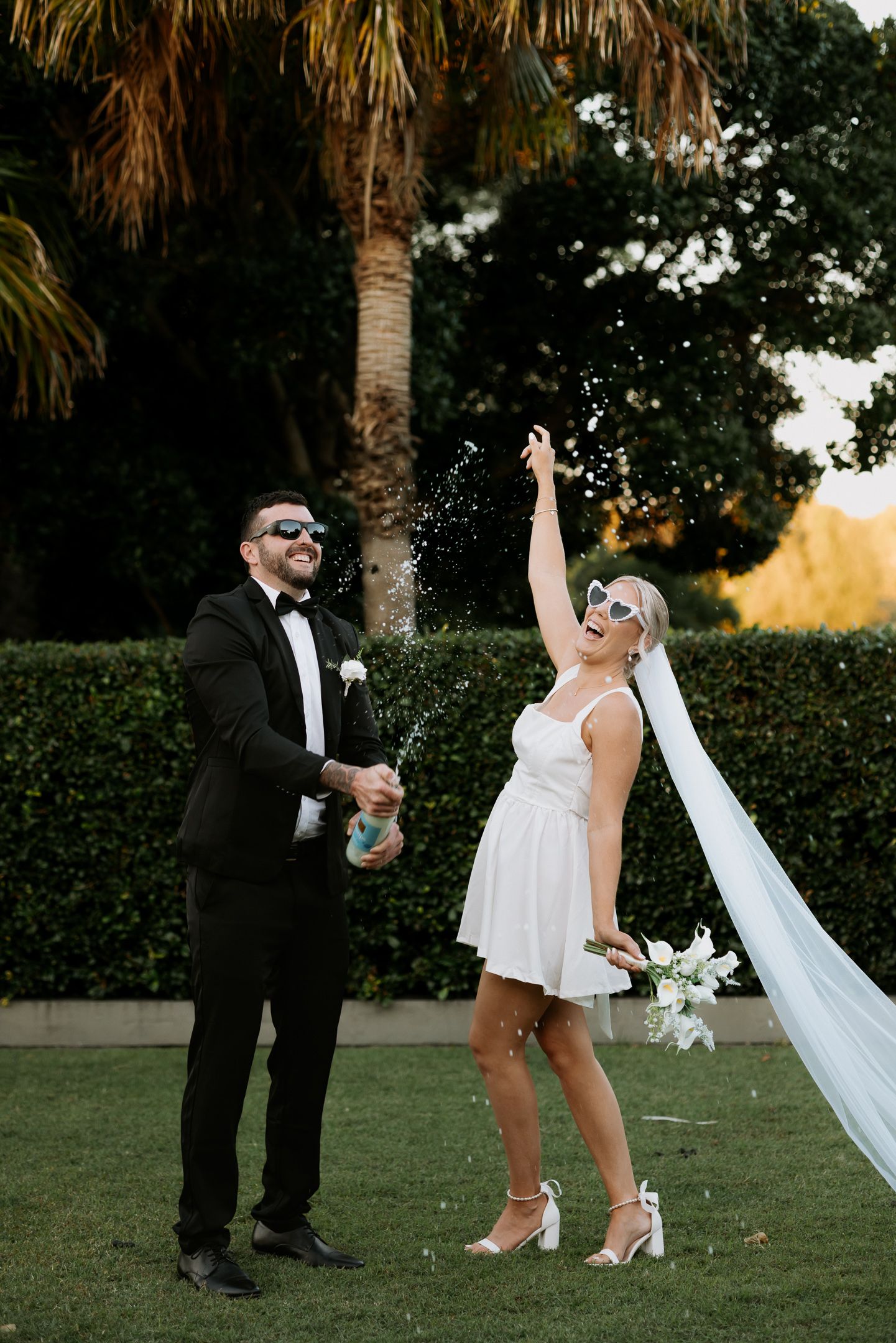 Playful wedding couple dances near palm trees at sunset.