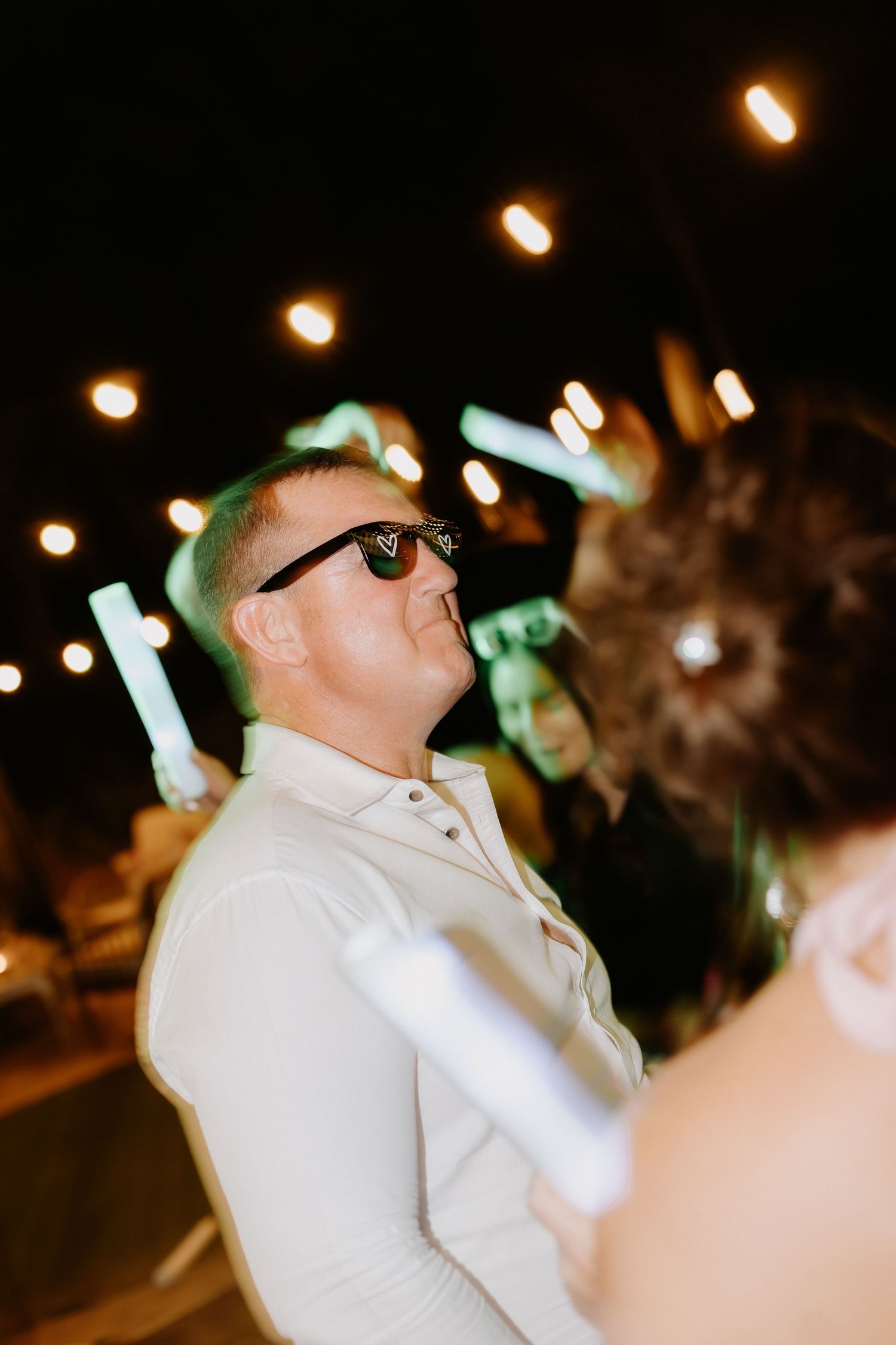 Guest wearing sunglasses enjoying nighttime celebration under string lights.
