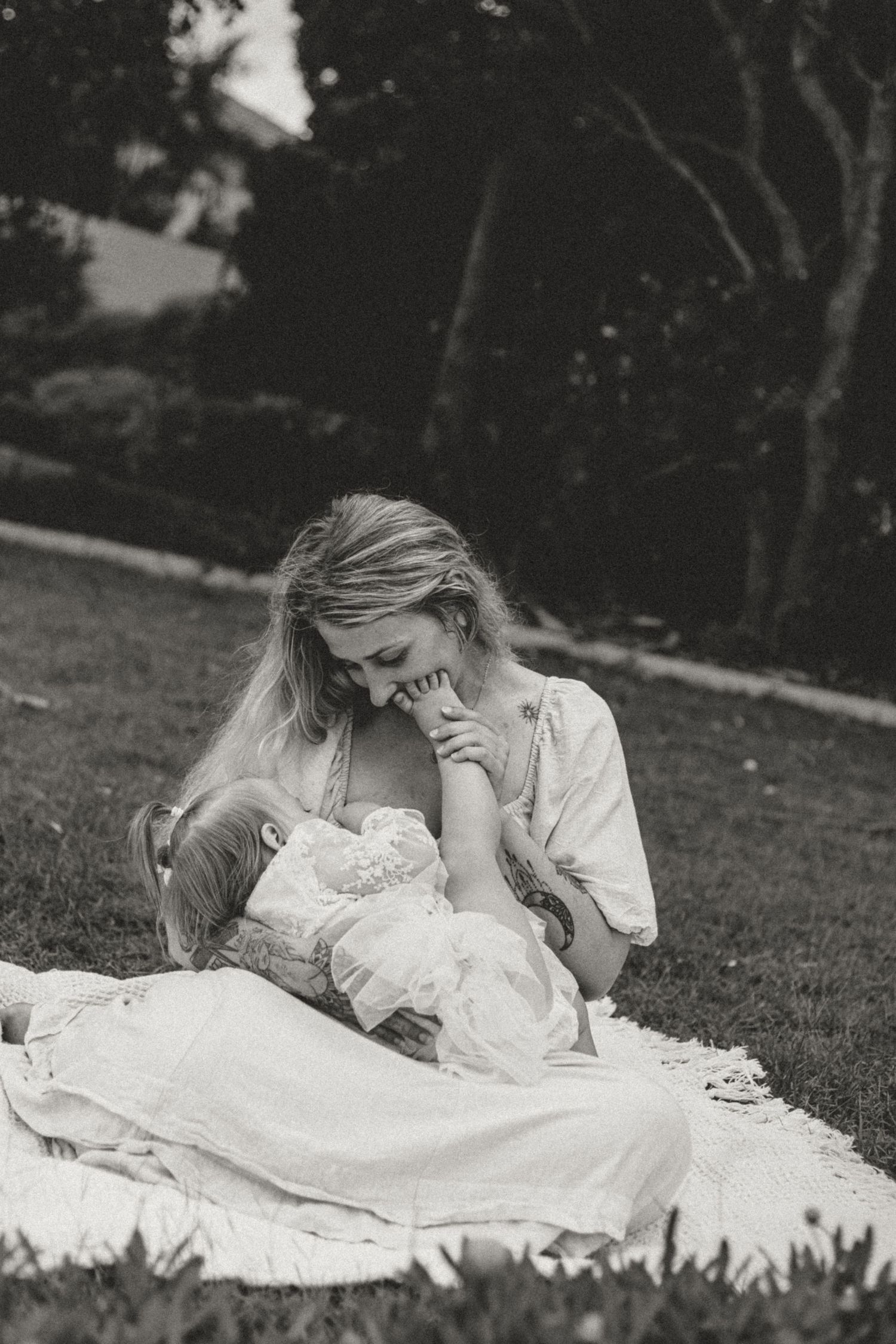 A black and white photo series shows a person in a white dress lying on grass in various relaxed poses.