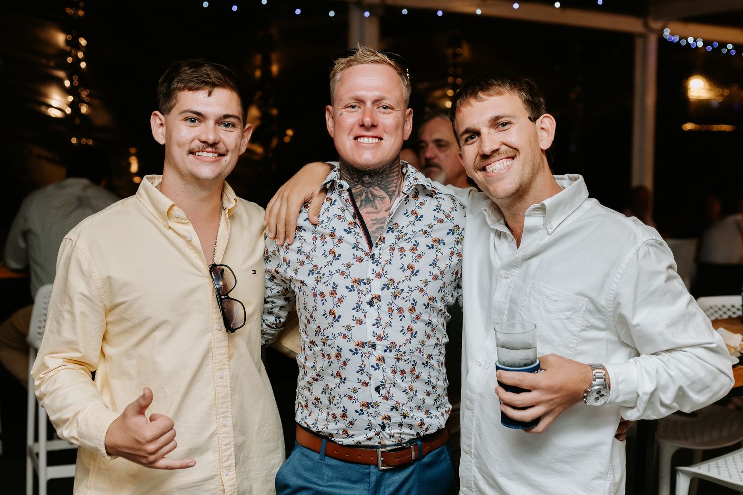 Three smiling men posing together at an outdoor wedding reception celebration at night.