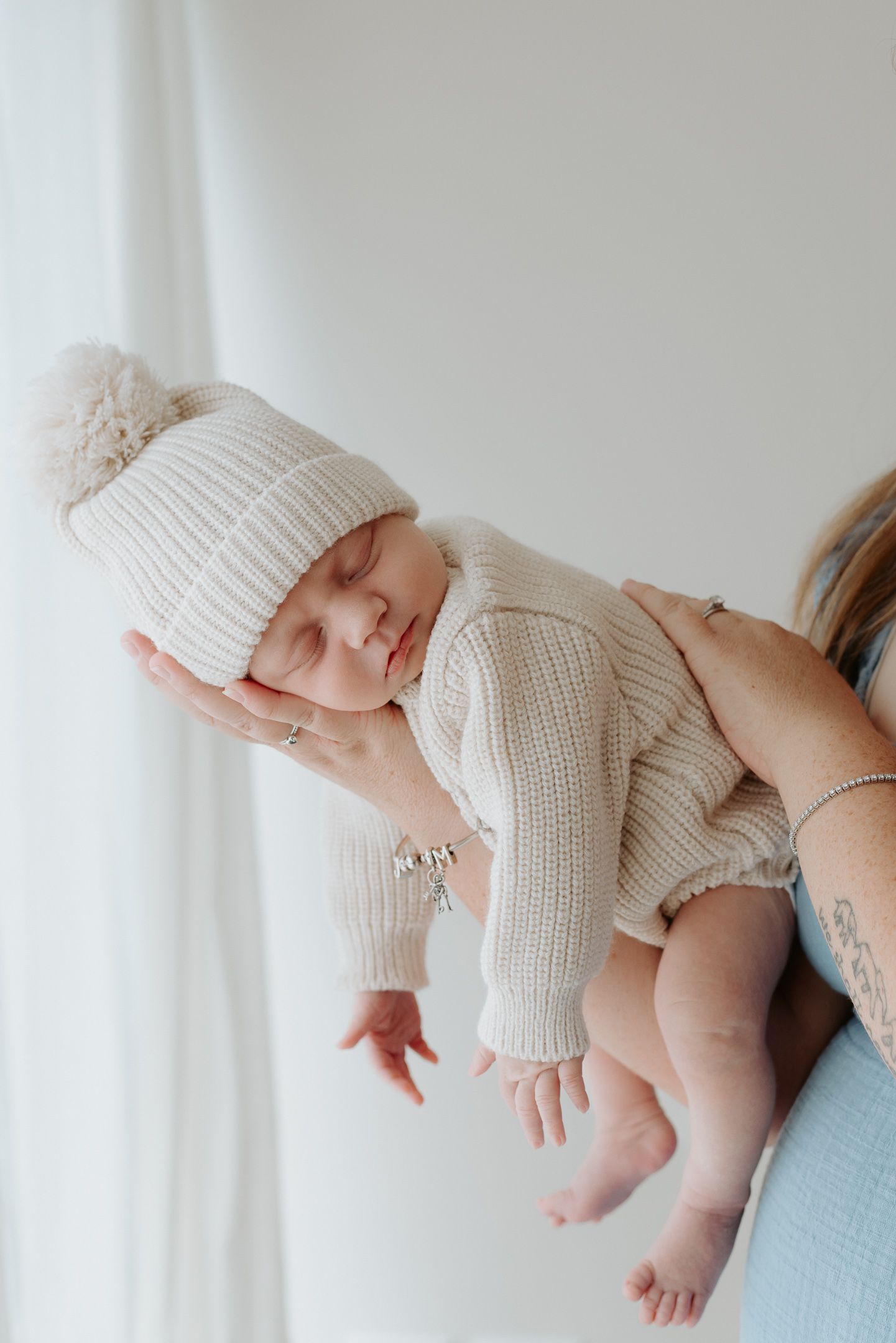 Sleeping baby wearing white knit sweater and hat lies on light blue blanket in soft natural light.