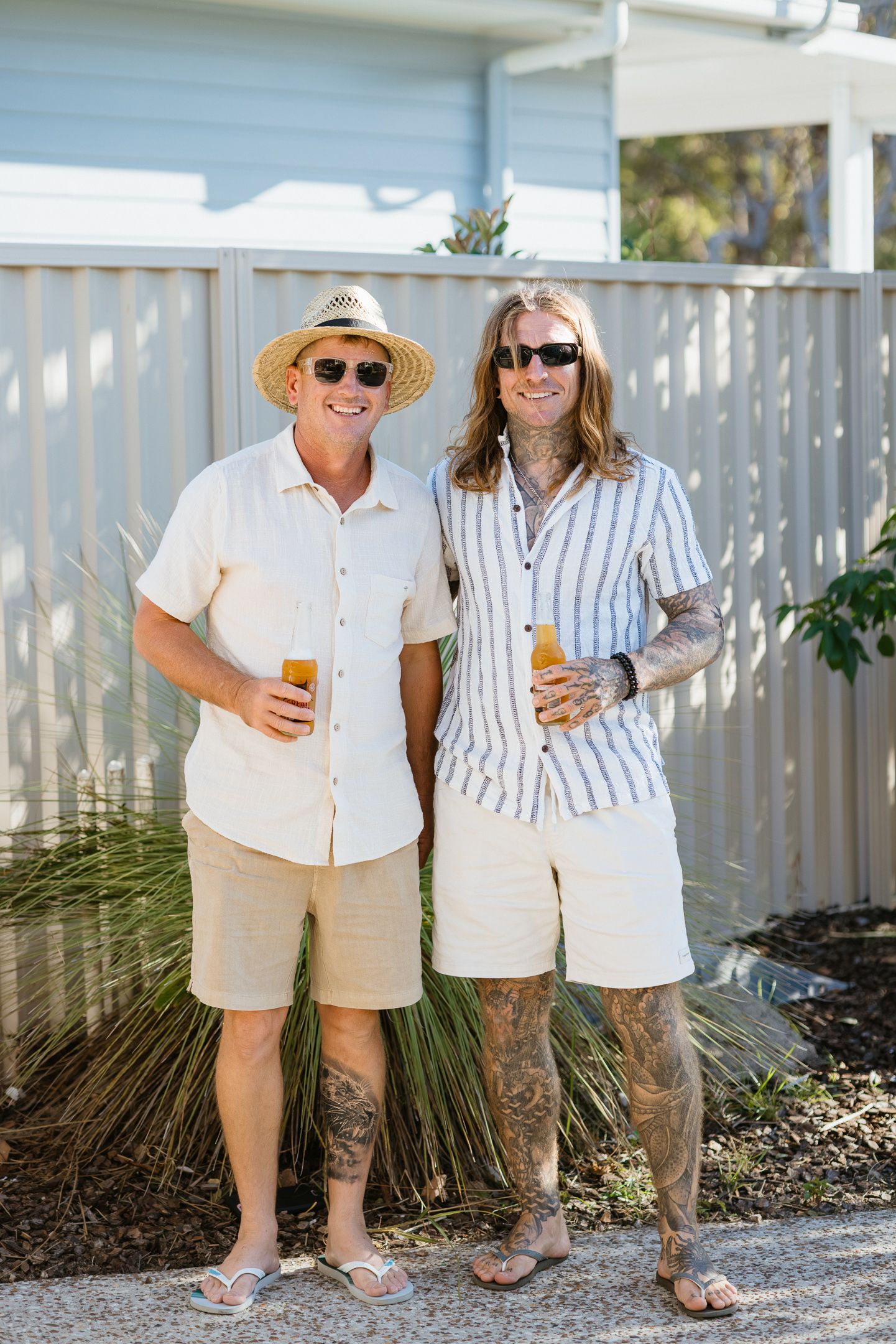 Two people in coordinated summer outfits standing together on a white pebble path next to a white picket fence.