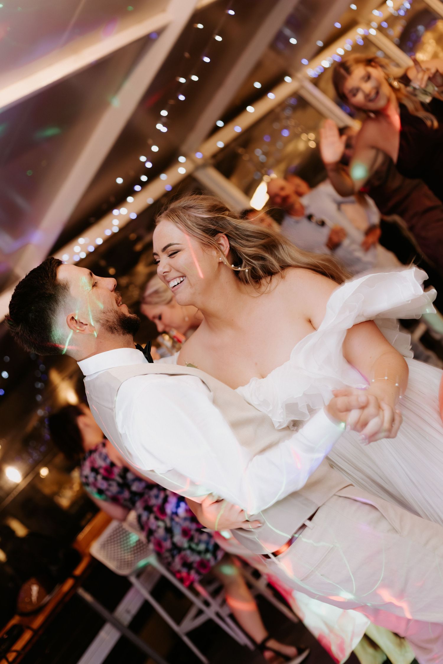 A joyful couple shares their first dance at a wedding reception under twinkling string lights.