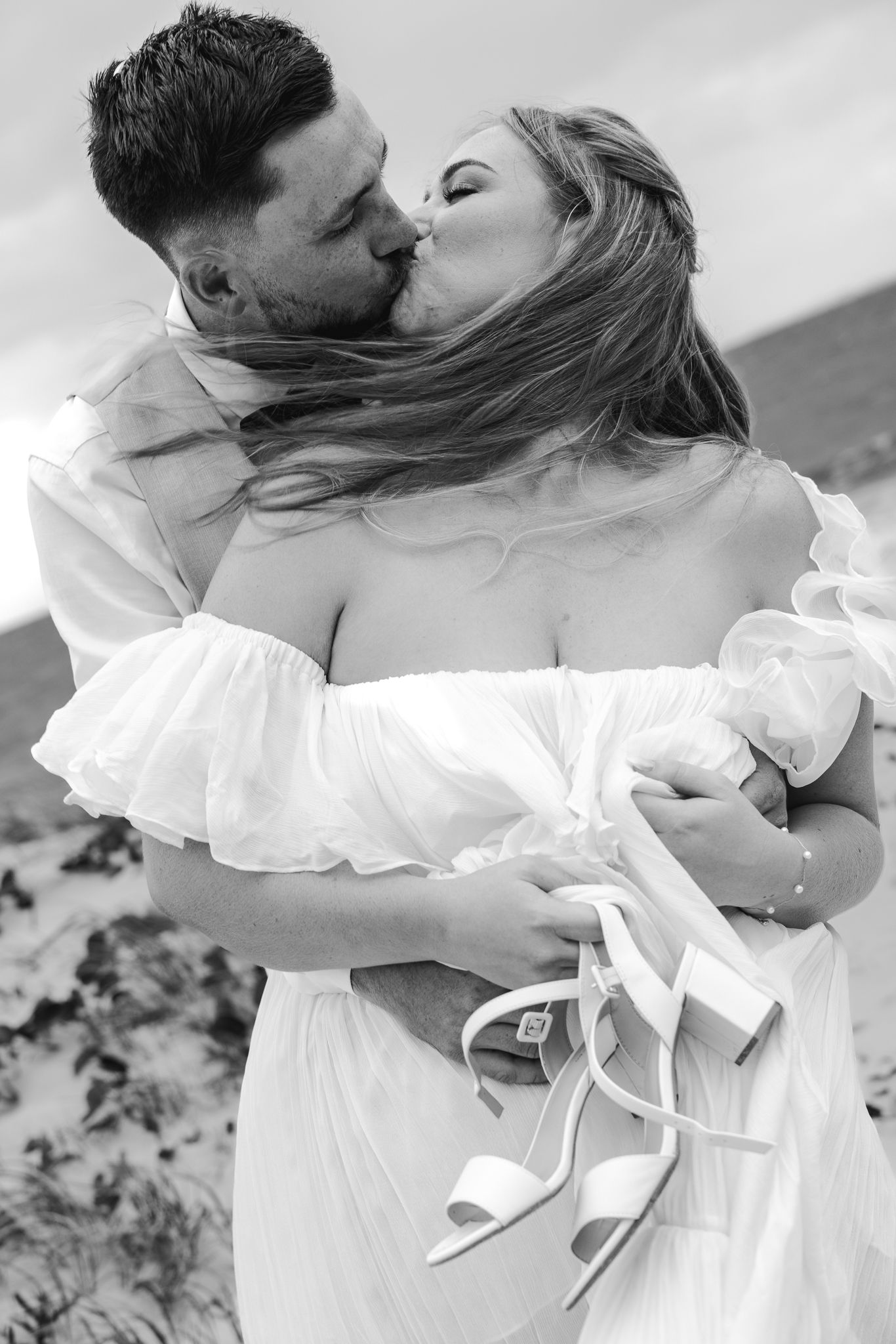 Black and white photo of bride and groom sharing a passionate kiss outdoors on their wedding day.