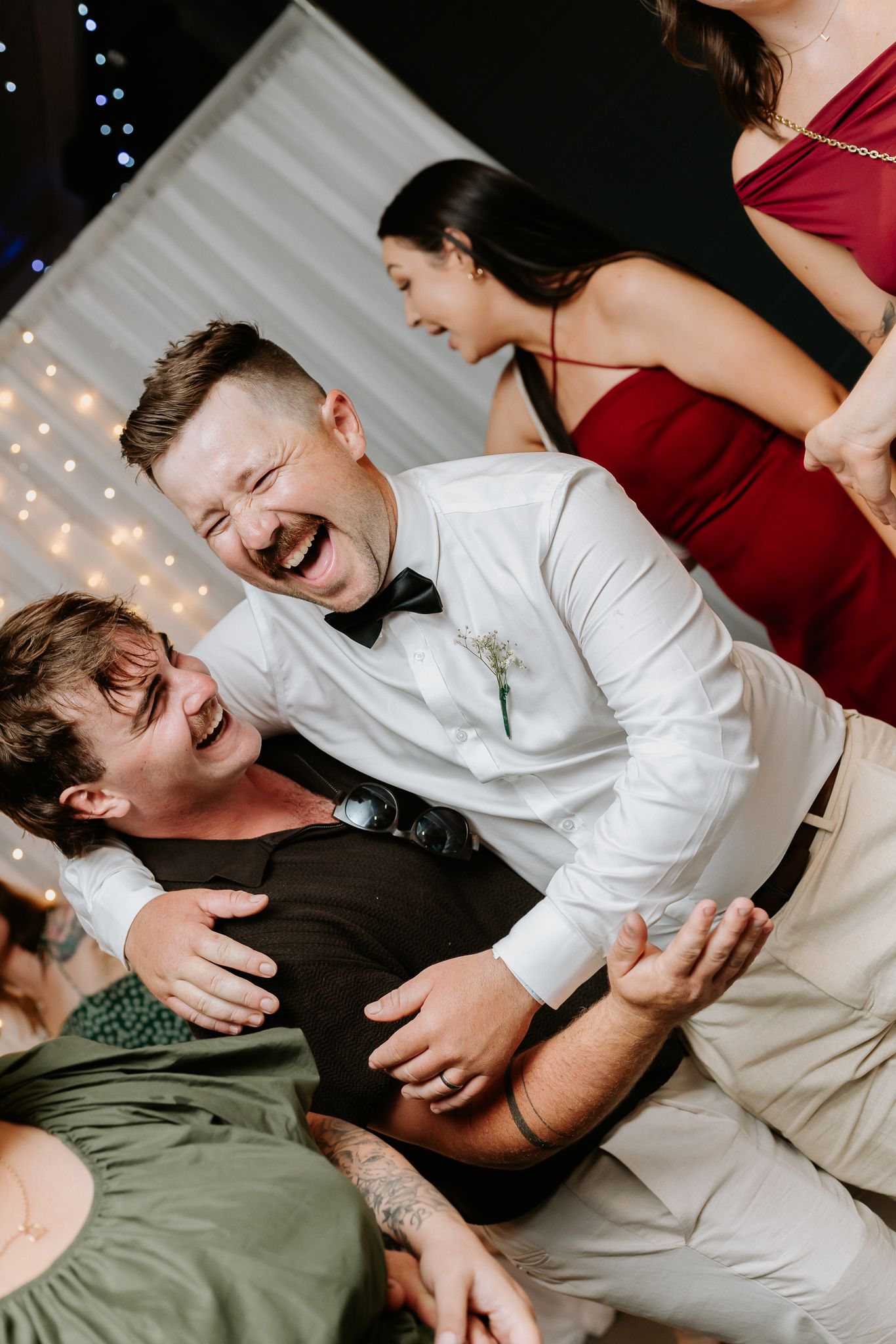 Groom in white shirt and bow tie laughing with a guest on the wedding dance floor.