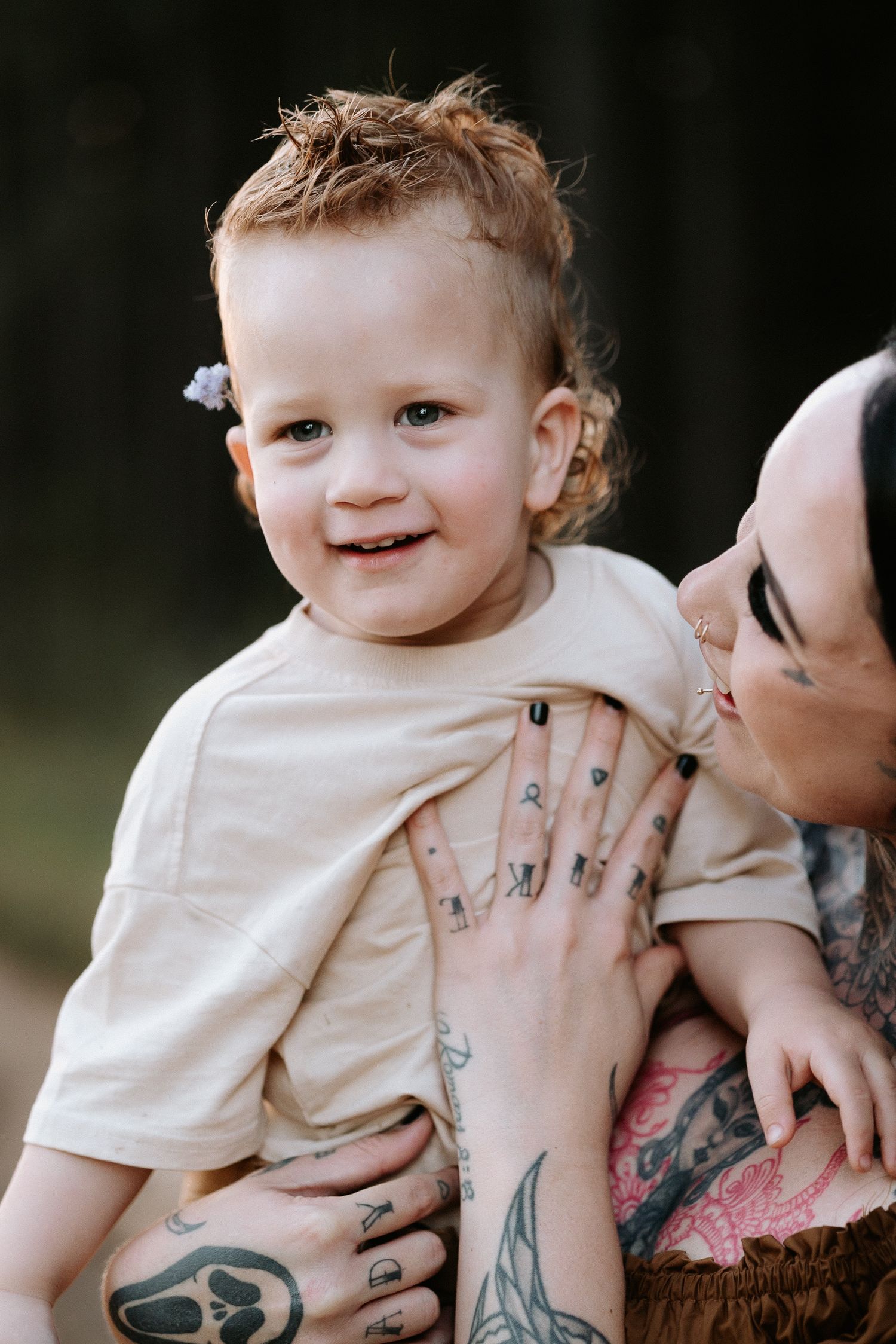 A series of four photos showing a baby in a cream-colored outfit being held by someone with visible arm tattoos.