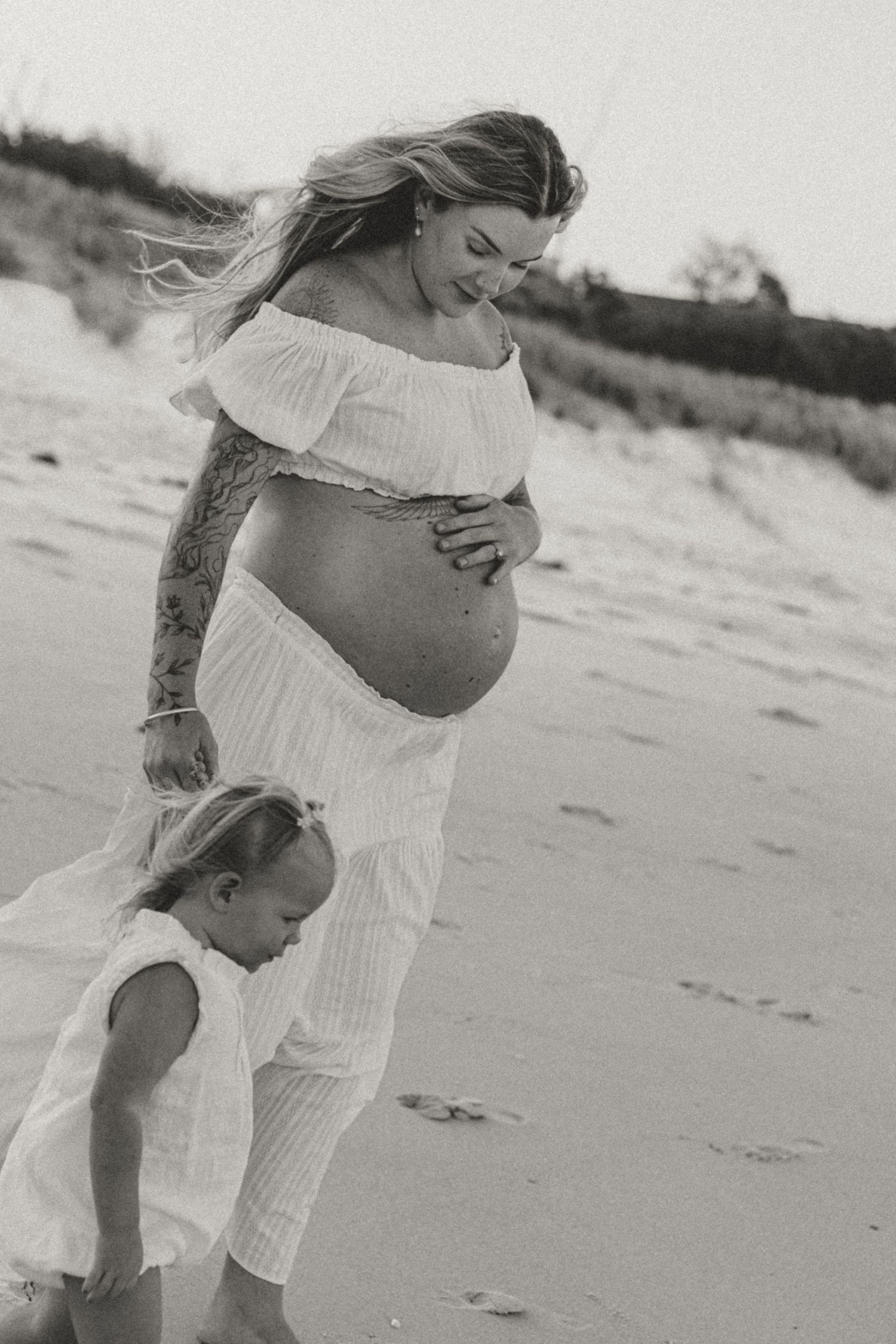 A series of black and white beach photos showing a pregnant woman in a white dress with a young child.