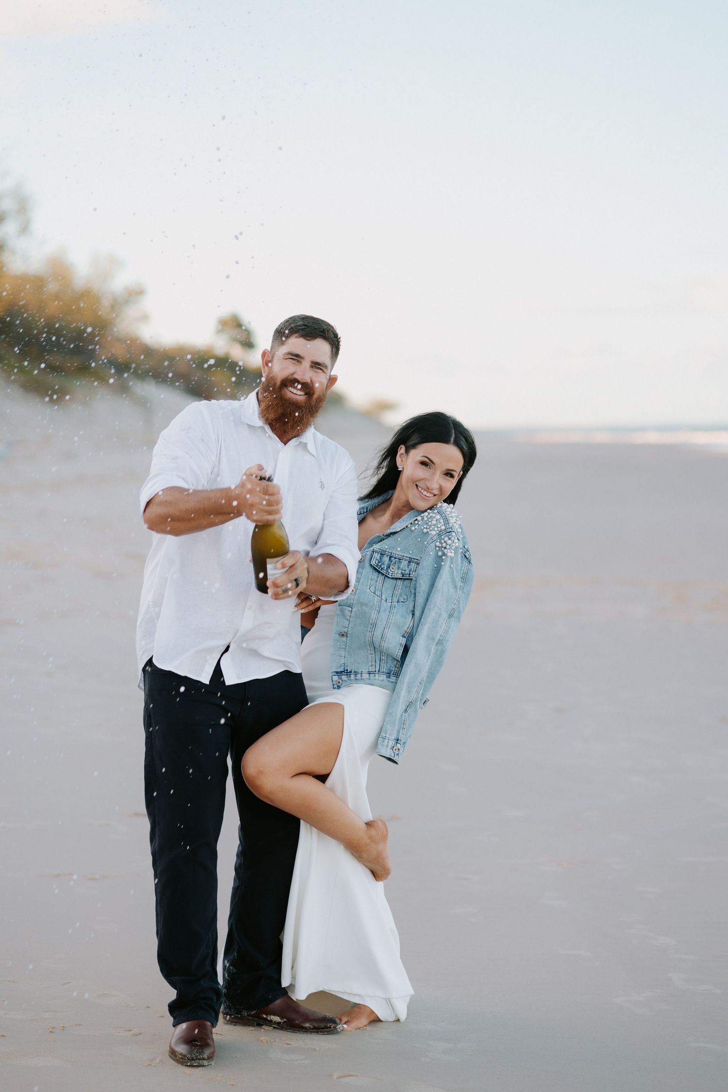 A playful couple dances together on a beach at sunset.