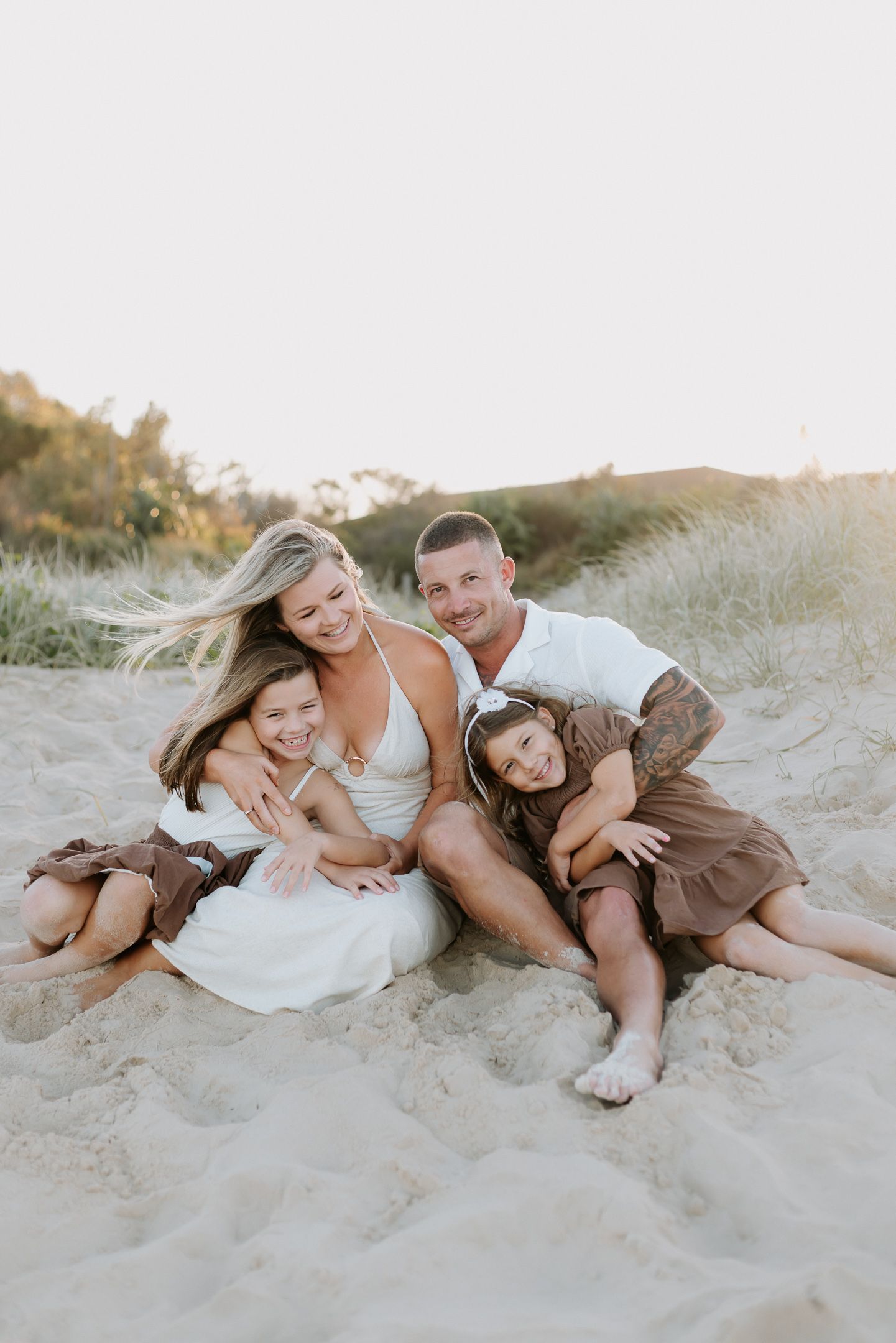 A family lounges together on a sandy beach during a warm sunset photoshoot.