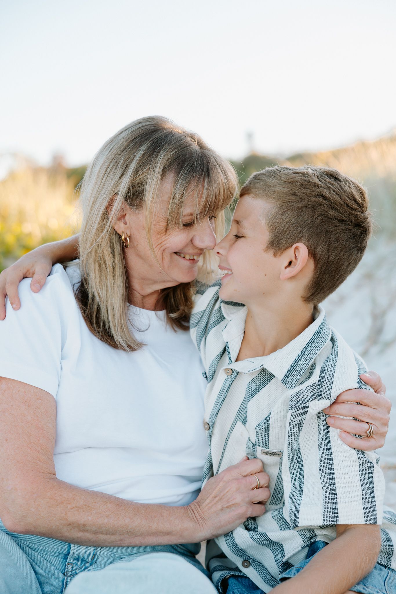 A woman and young boy share a tender moment smiling at each other on a beach.
