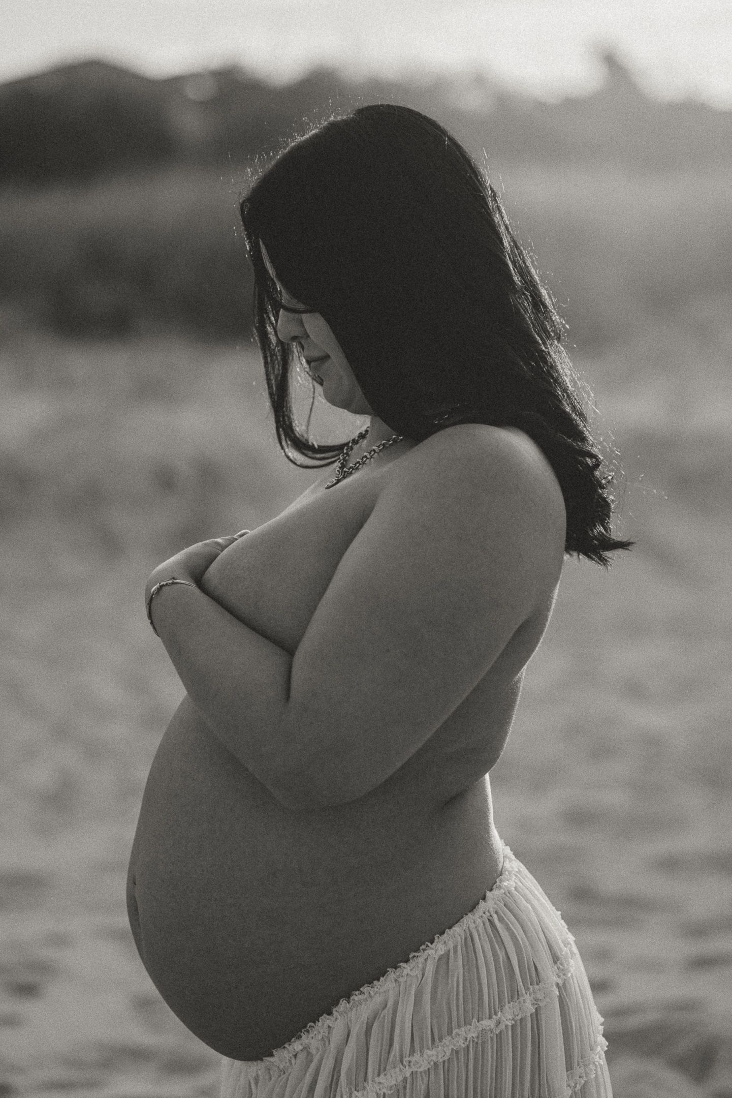 Black and white artistic maternity photo series showing a pregnant woman in a white dress on a beach at sunset.