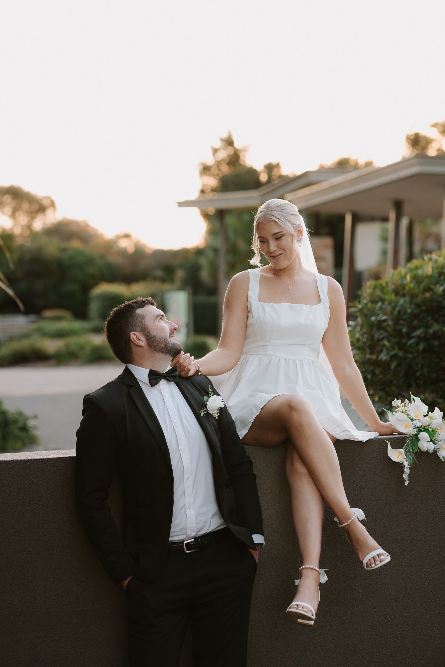 Couple shares relaxed moment sitting on wall at sunset.