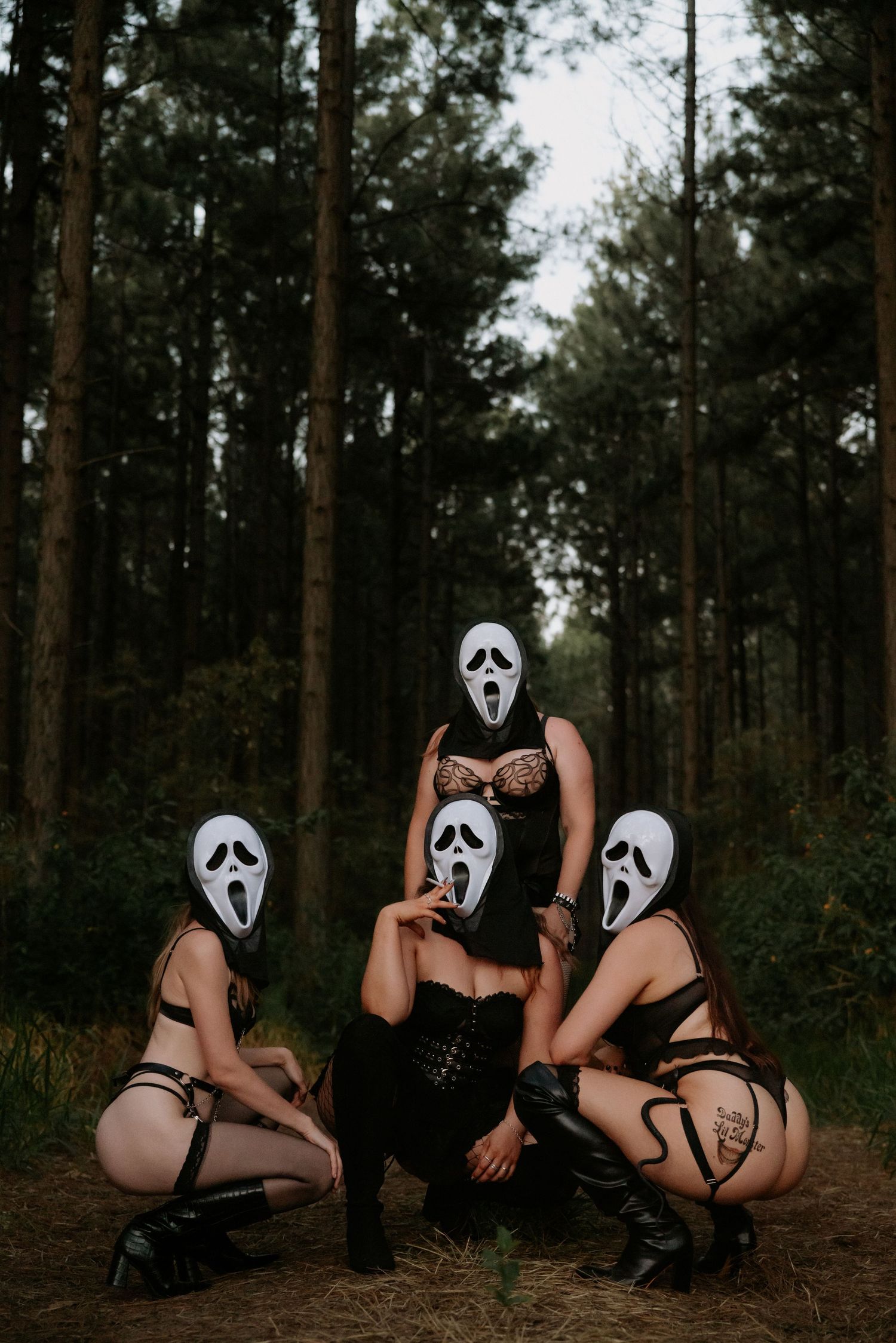 Three women in lingerie and Ghostface masks pose dramatically in a dark forest setting.