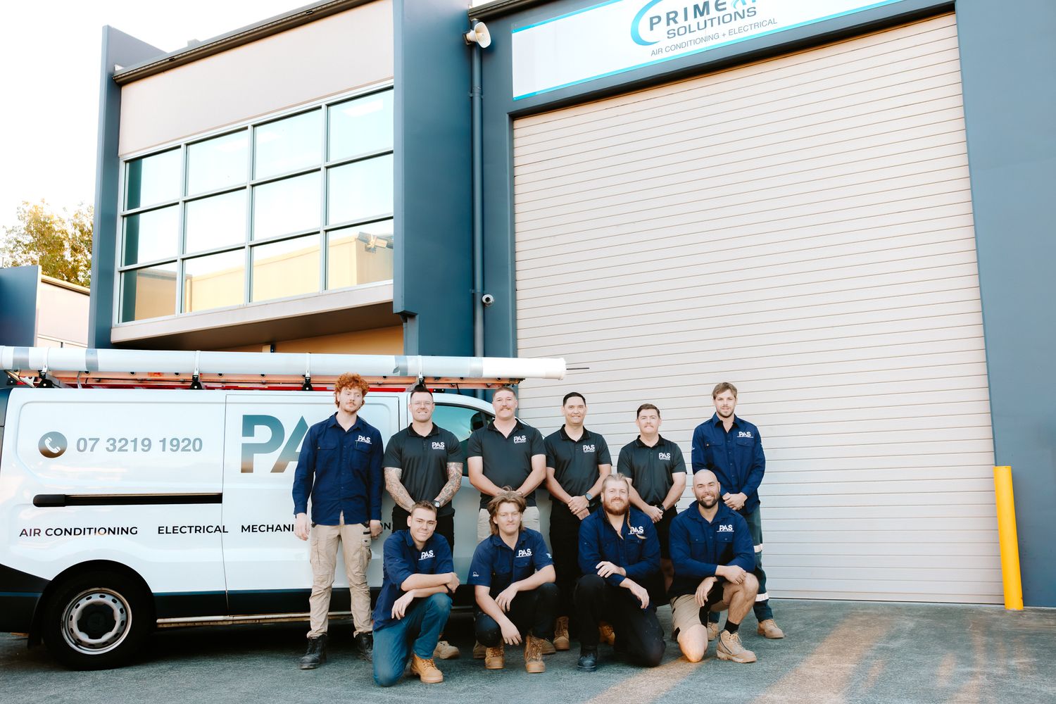 Prime Solutions team of technicians posing outside their commercial workshop with a branded service van in Australia.