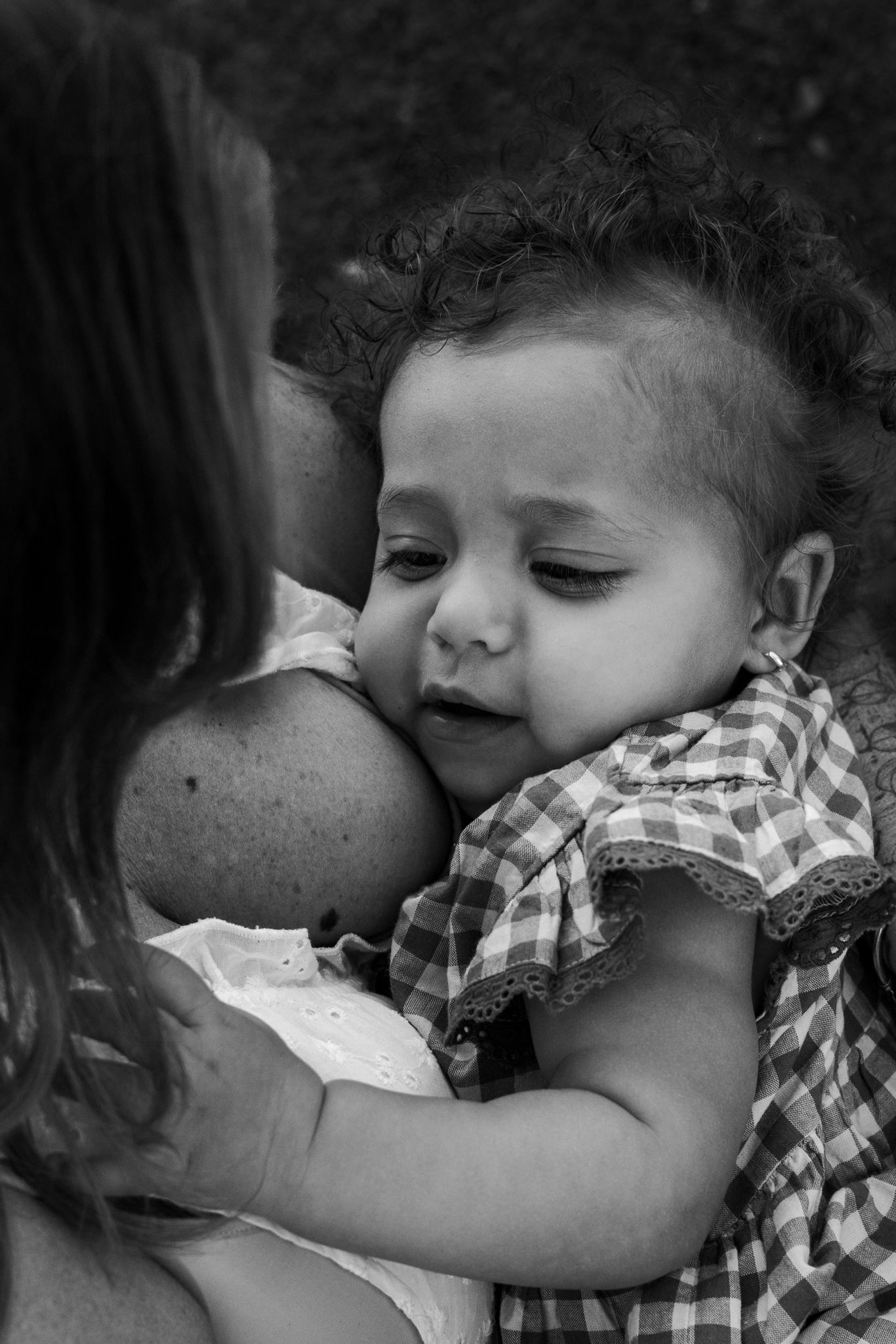 Black and white photo of a curly-haired baby in plaid dress being held and comforted by a woman.