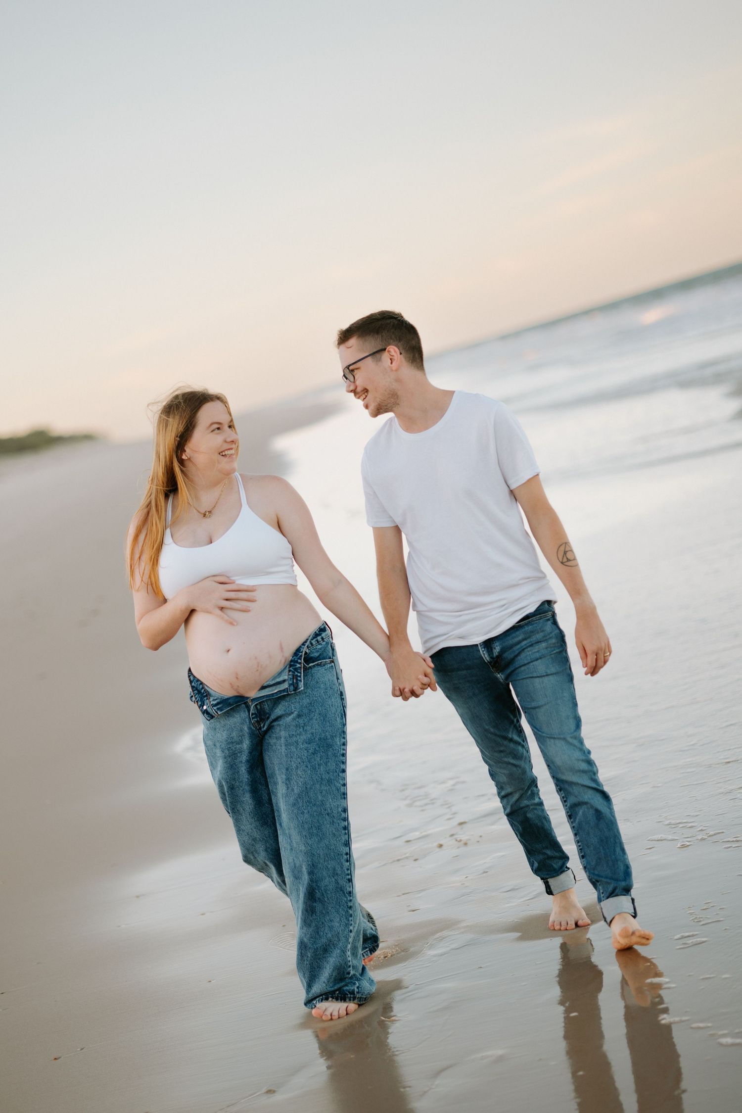 A couple playfully walks along the beach at sunset, splashing in the shallow water and holding hands.