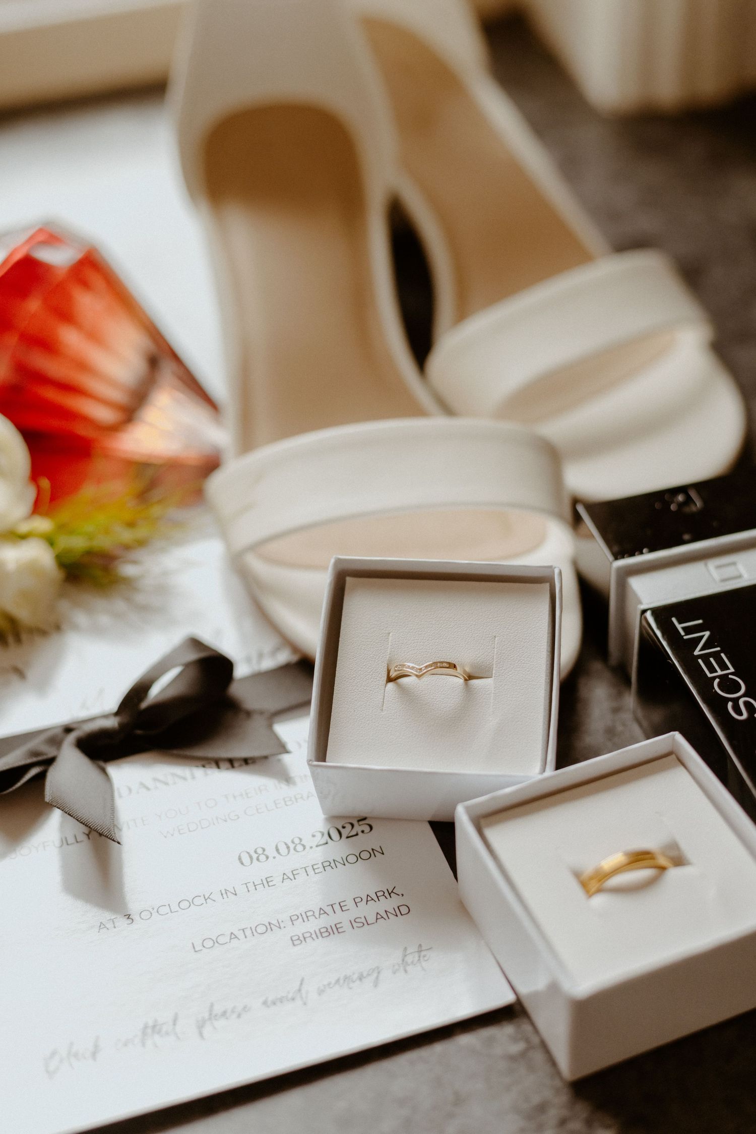 Wedding details including white bridal shoes, jewelry boxes, and golden rings arranged on a light surface.
