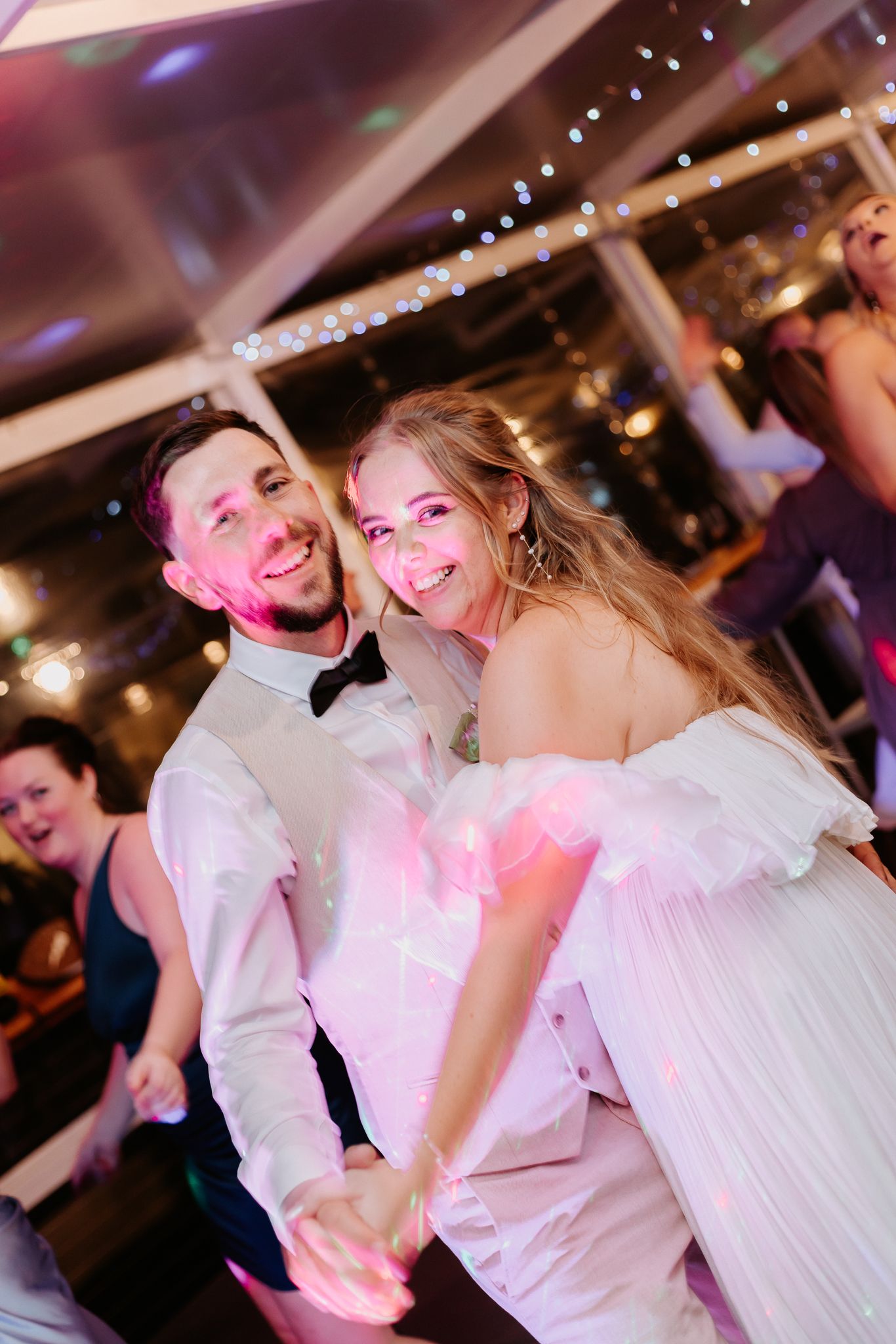 Smiling bride and groom dancing together at their wedding reception under fairy lights.