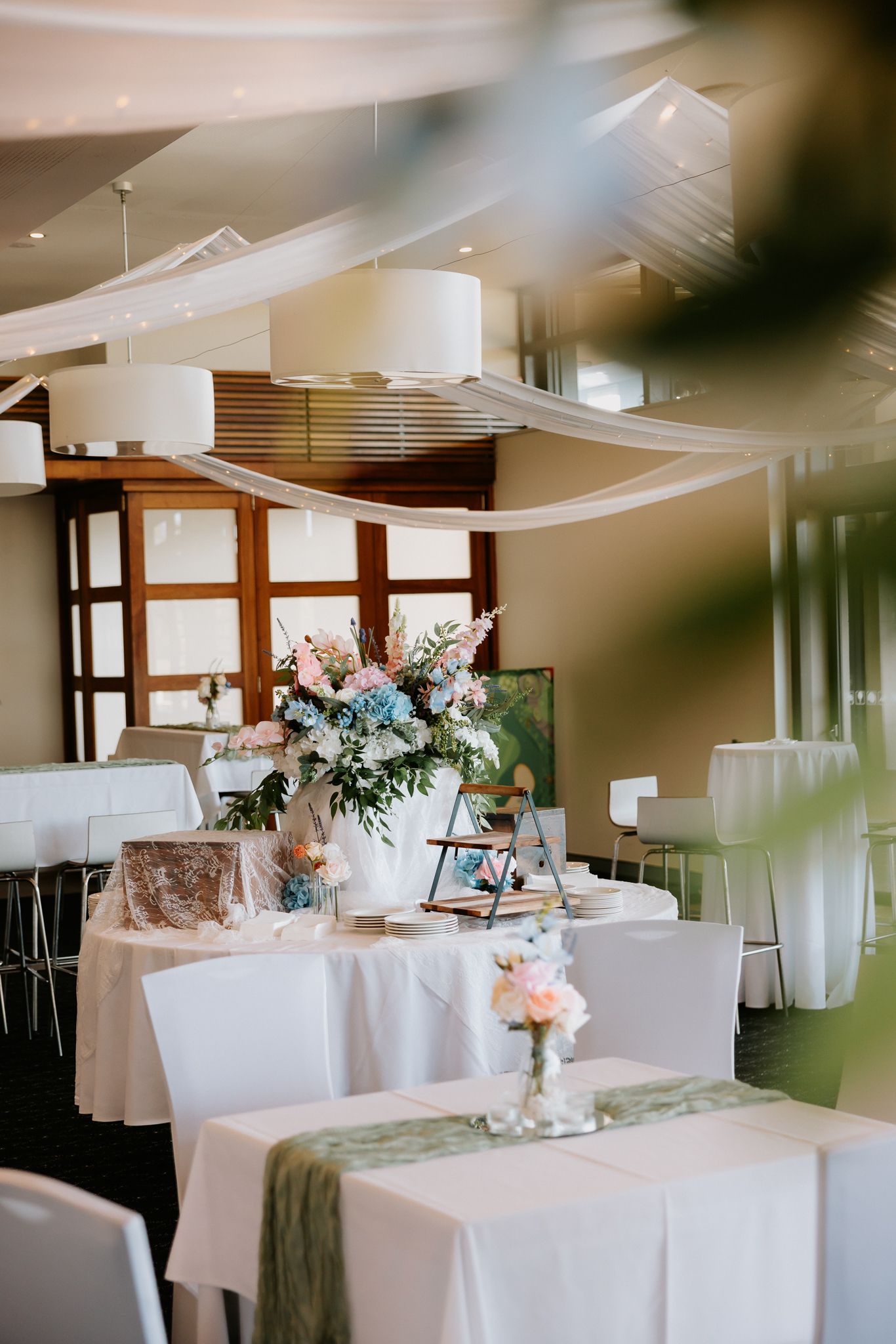 Elegant wedding reception venue with white draped ceilings, floral centerpieces in pink and blue, and white tablecloths.