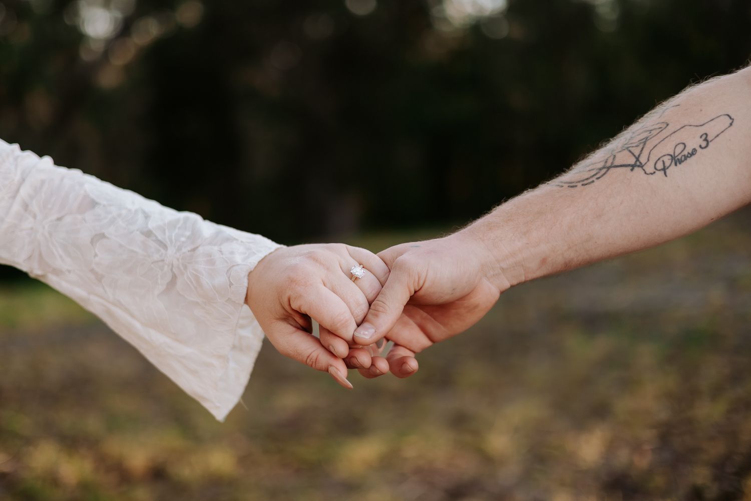 Close-up of a couple holding hands outdoors, one wearing a lace sleeve and the other with a hand tattoo.