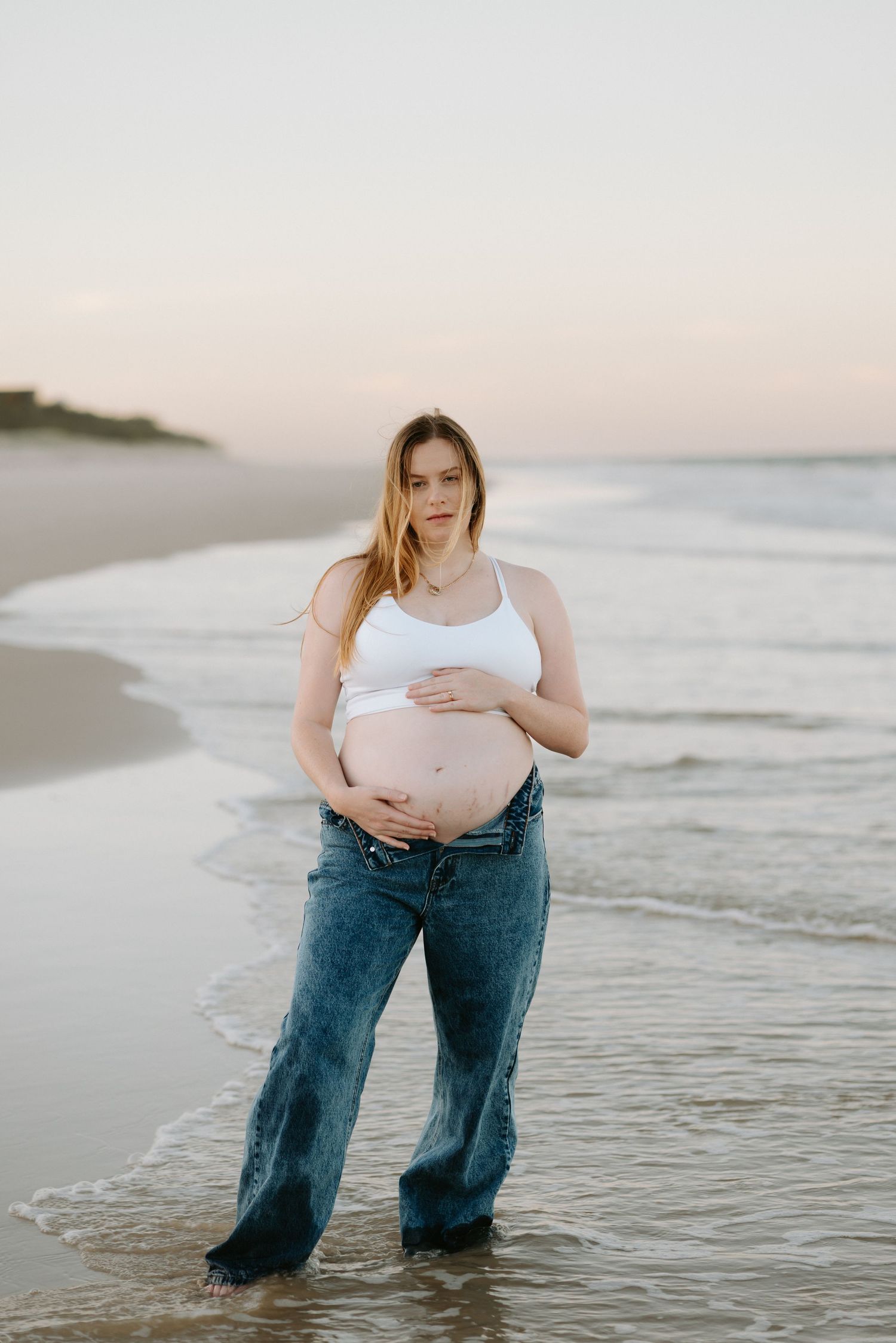 Person wearing jeans stands in shallow ocean water at sunset creating a dreamy beach scene.