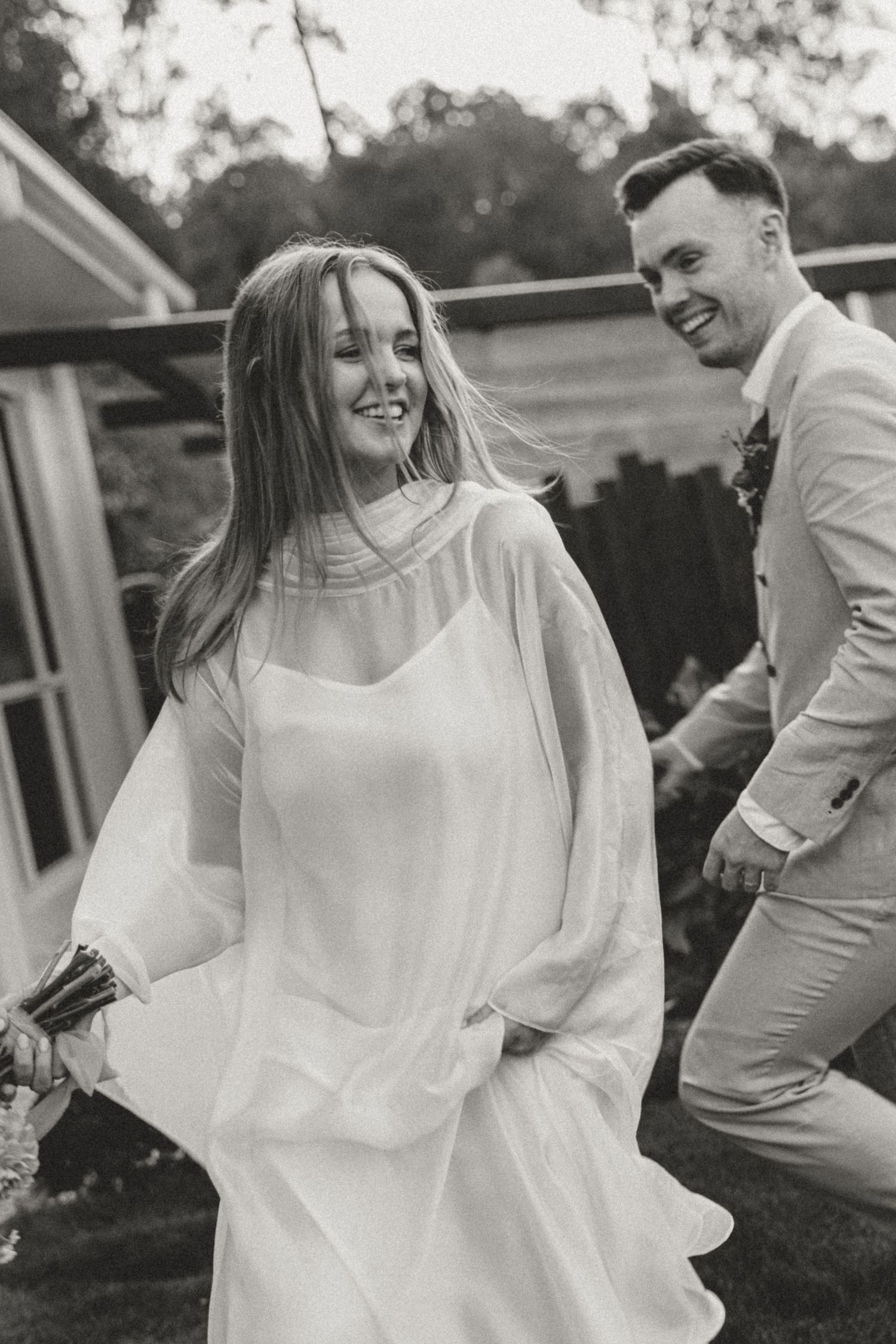 Black and white candid photo of a couple in flowing white and beige attire.