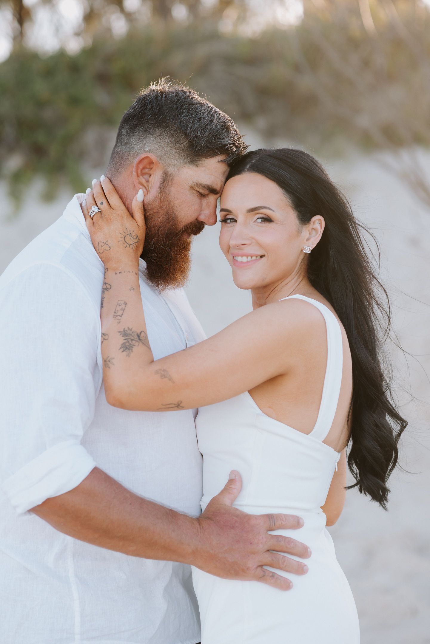 A romantic beach portrait of a couple in white outfits embracing during sunset, with soft natural lighting.