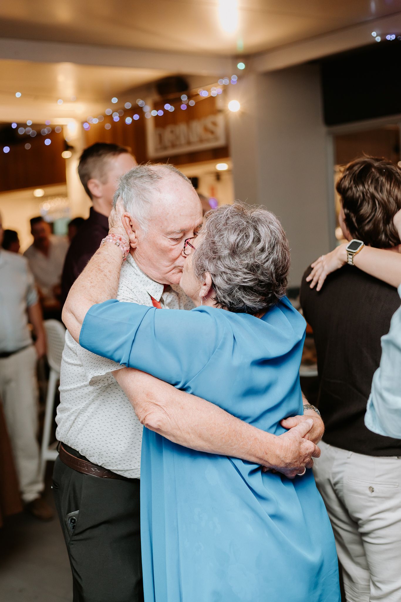 Elderly couple sharing a romantic kiss while dancing at a wedding reception.
