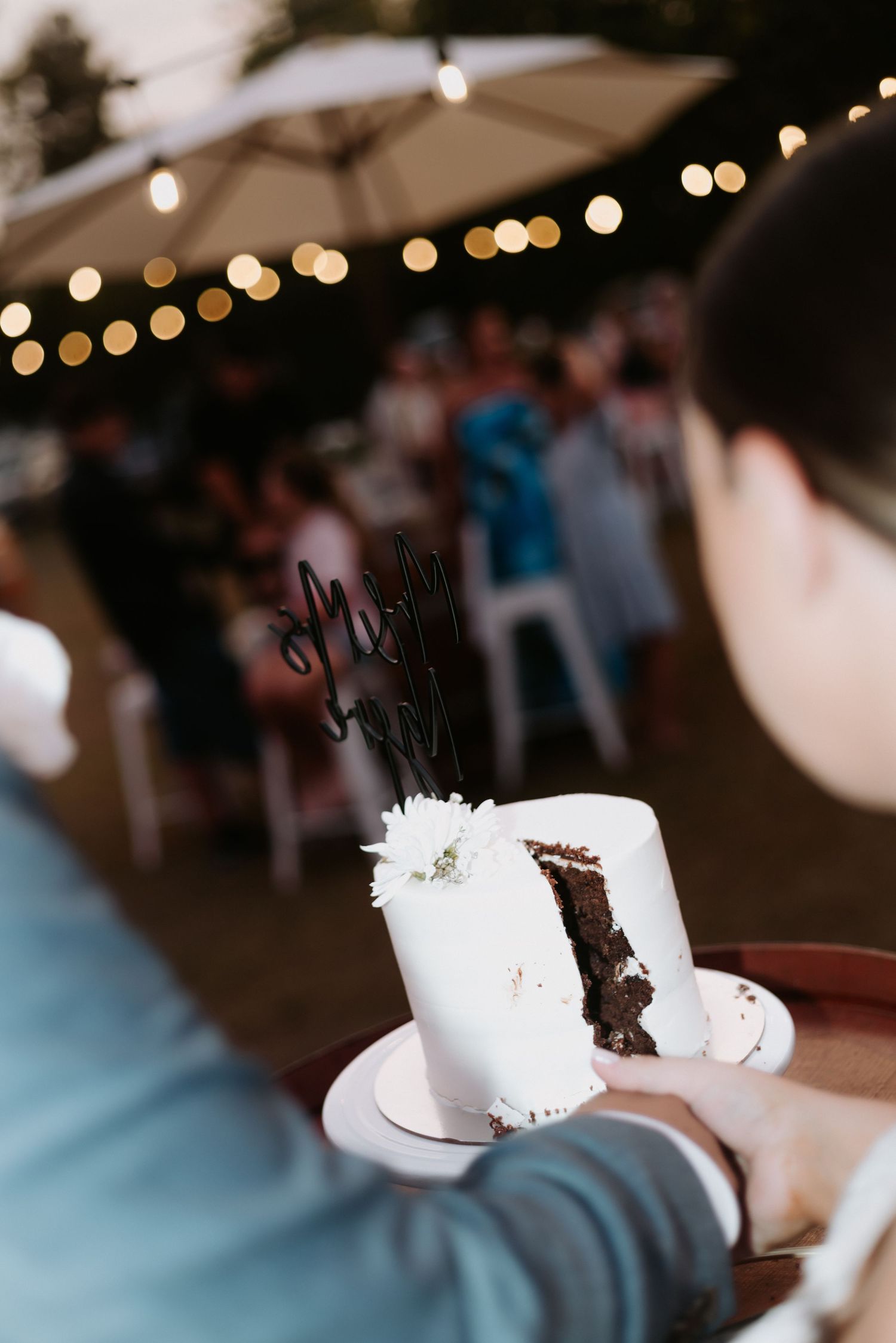 A close-up shot of wedding cake being cut with bokeh lights in the background during an indoor reception.