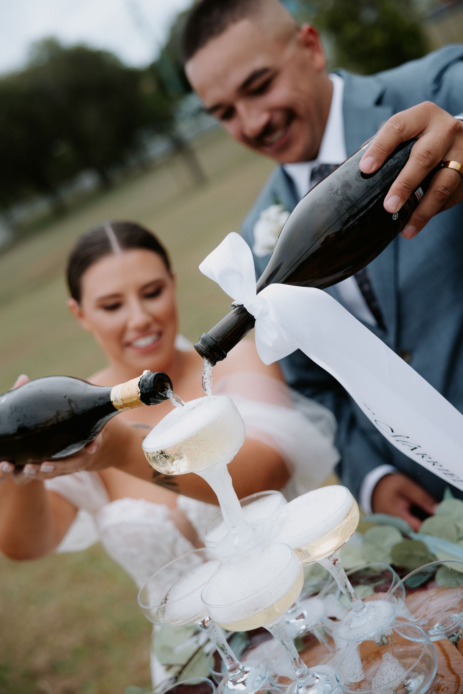 Newlyweds pour champagne together in a celebratory toast outdoors.