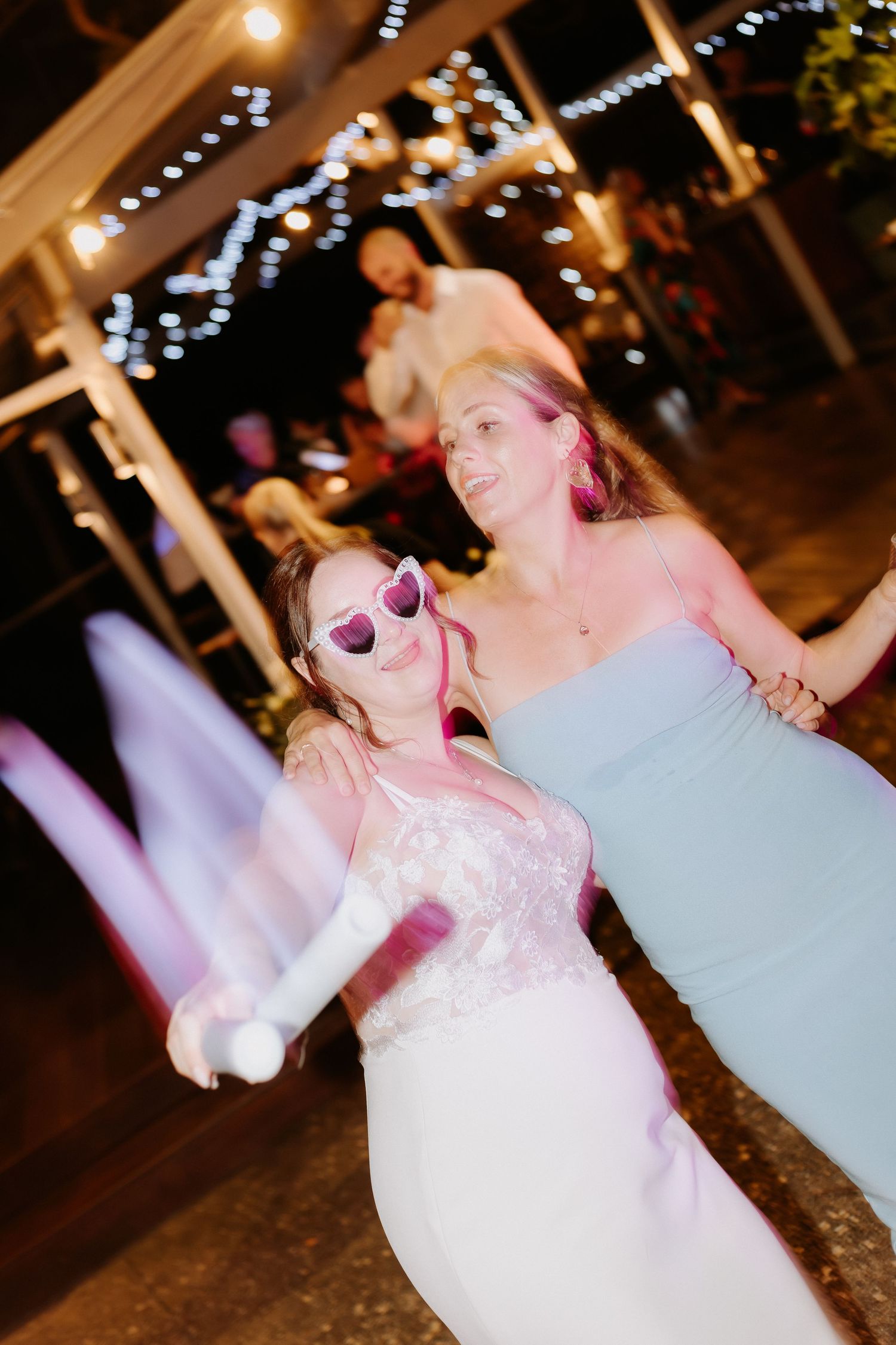 Wedding party dancing under twinkling lights at outdoor reception venue.