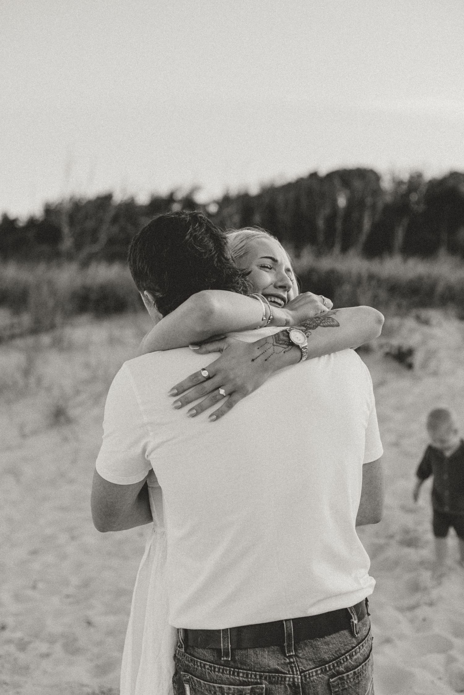 Black and white photo of a couple embracing on a sandy beach, woman smiling with arms around mans neck.