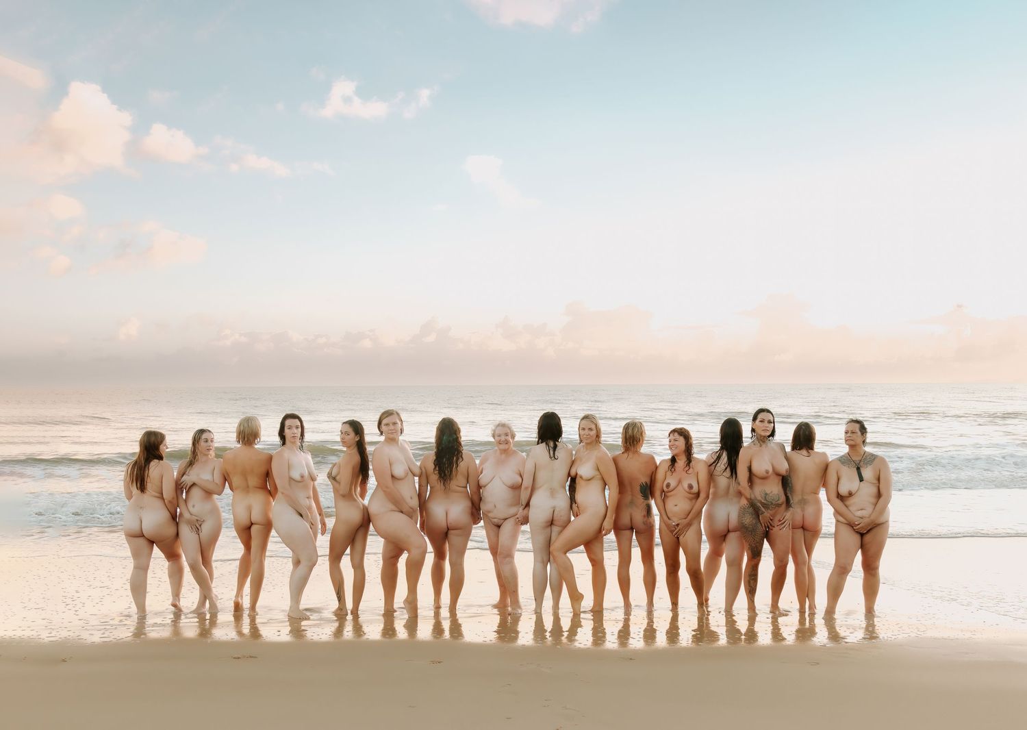 Group of women posing together on a sandy beach at sunset with ocean waves in the background.