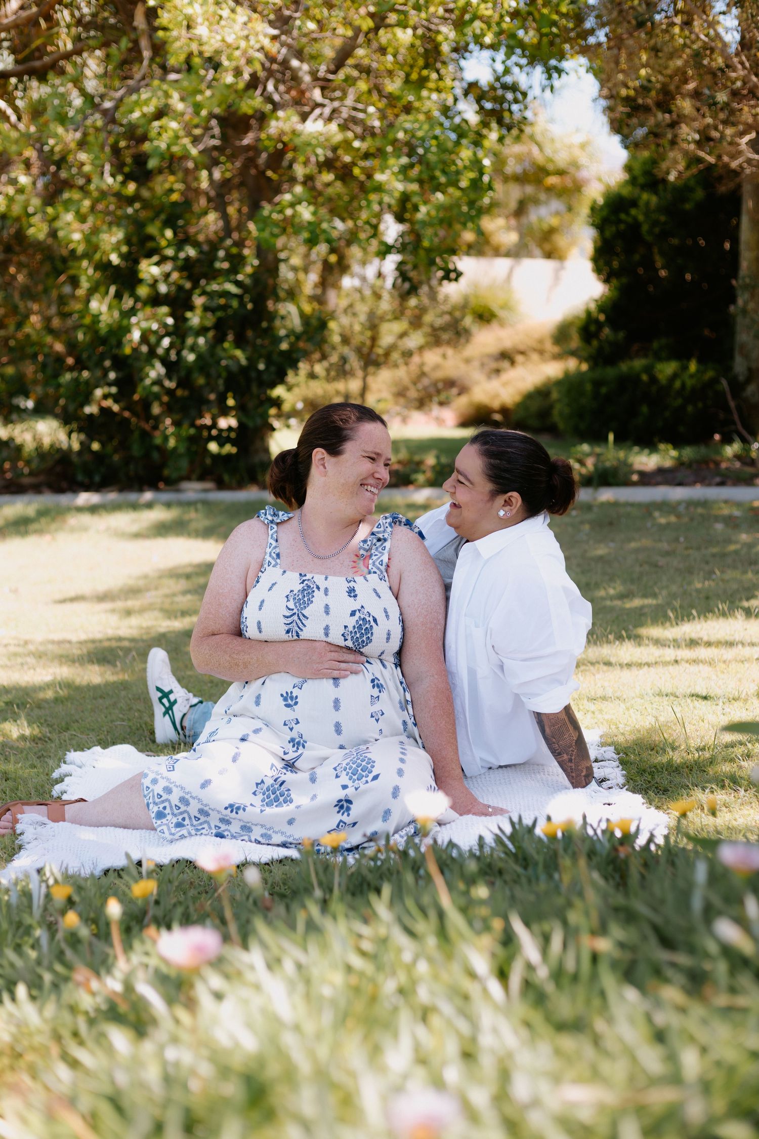 A couple shares a tender moment while lying on grass during a sunny outdoor photoshoot.