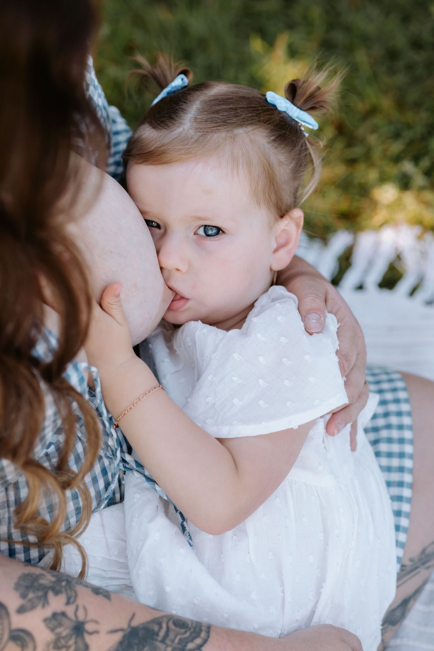 A small child in a white dress with blue hair bows embraces someone wearing a gingham dress.