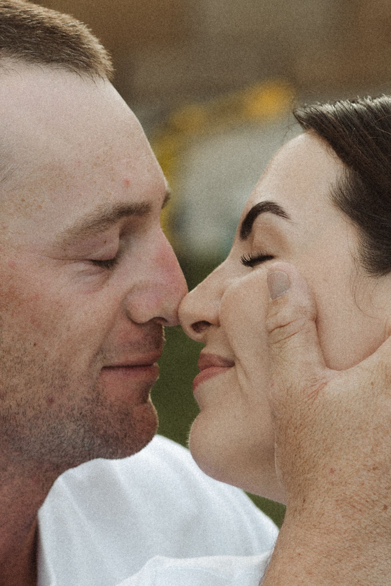 A romantic couple sharing an intimate moment, touching noses with eyes closed in a tender embrace outdoors.