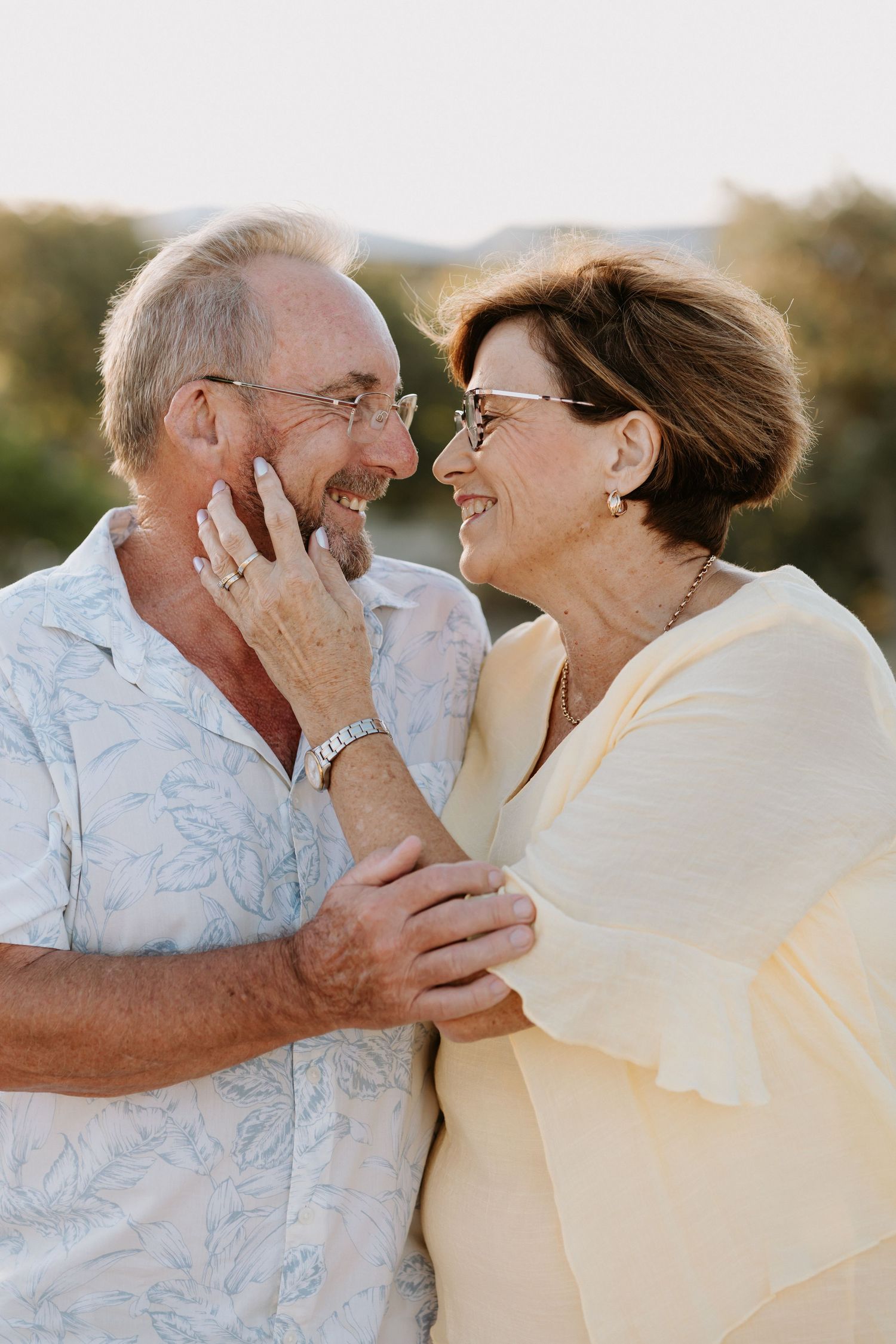 An elderly couple smiling and embracing outdoors, sharing a joyful moment together in warm golden light.