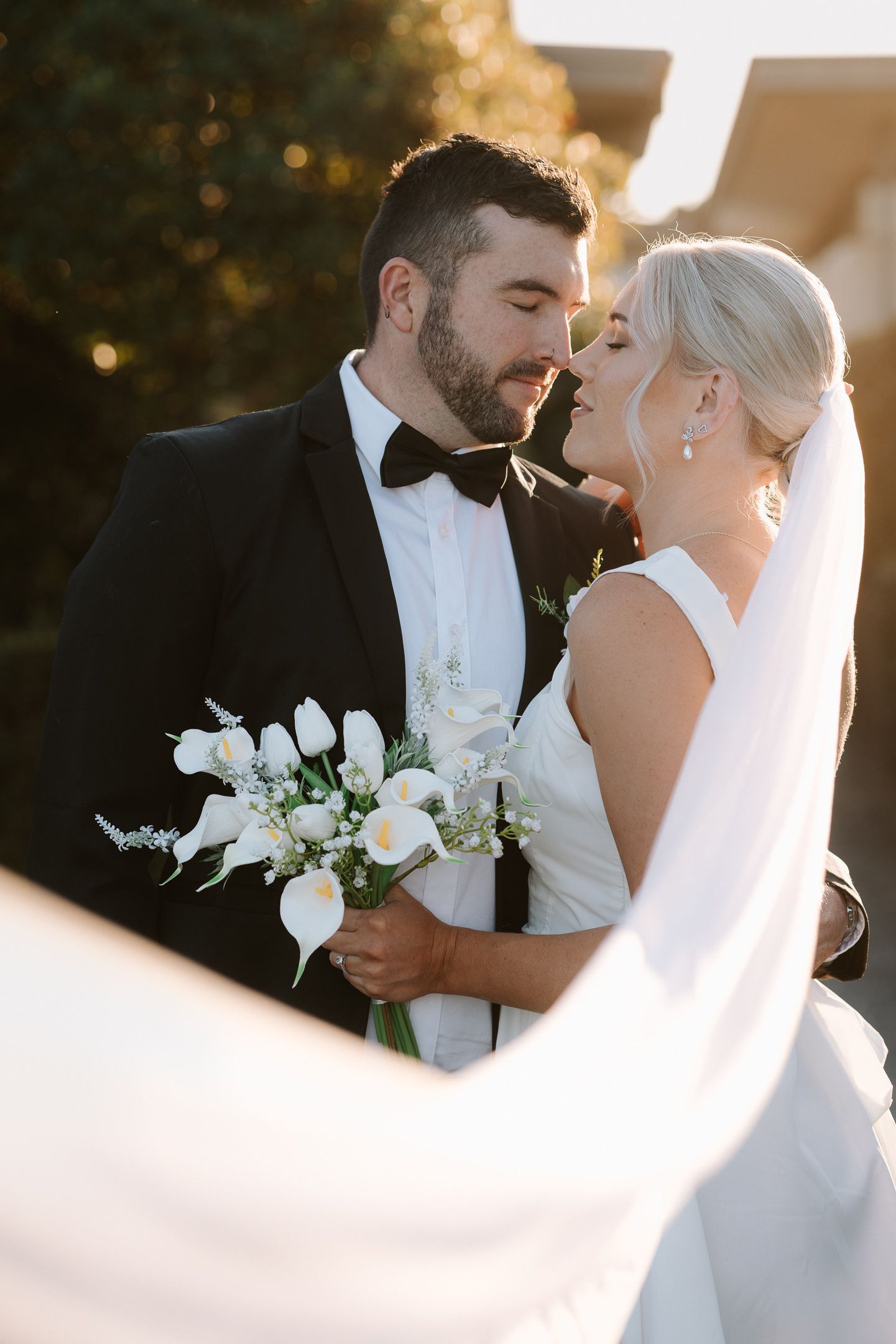 Romantic wedding couple shares intimate moments in golden sunlight with white orchid bouquet.