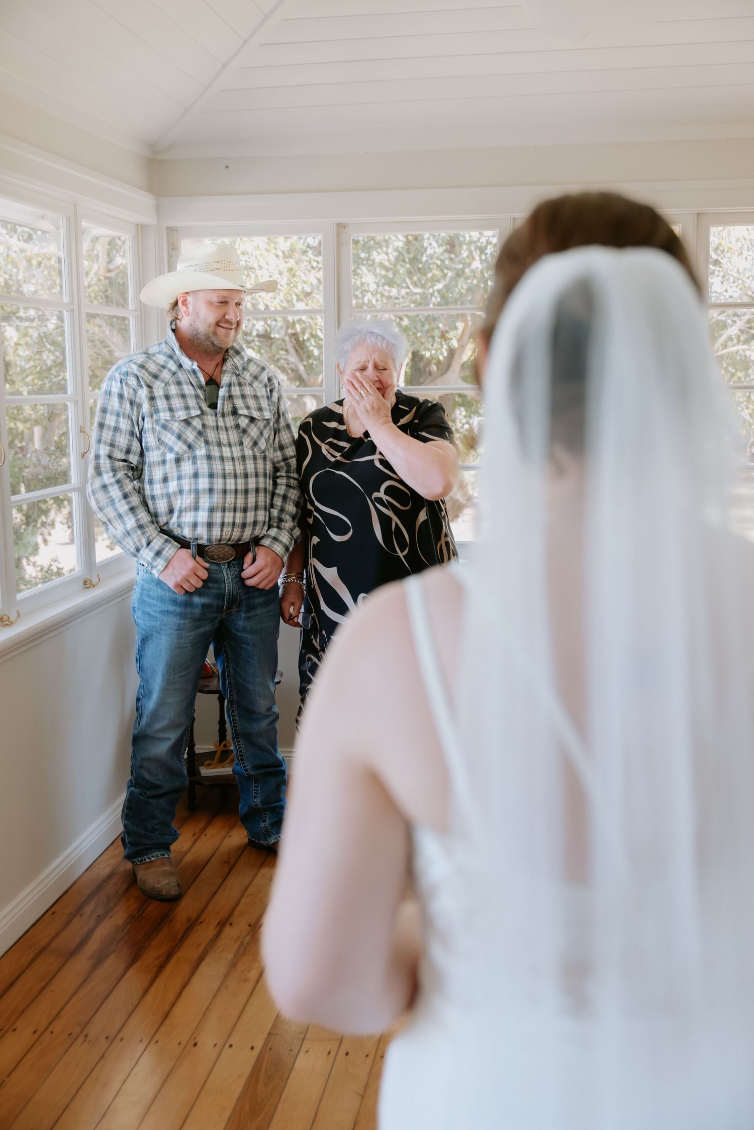 Emotional first look moment between bride and guest in a bright sunlit room with wooden floors.