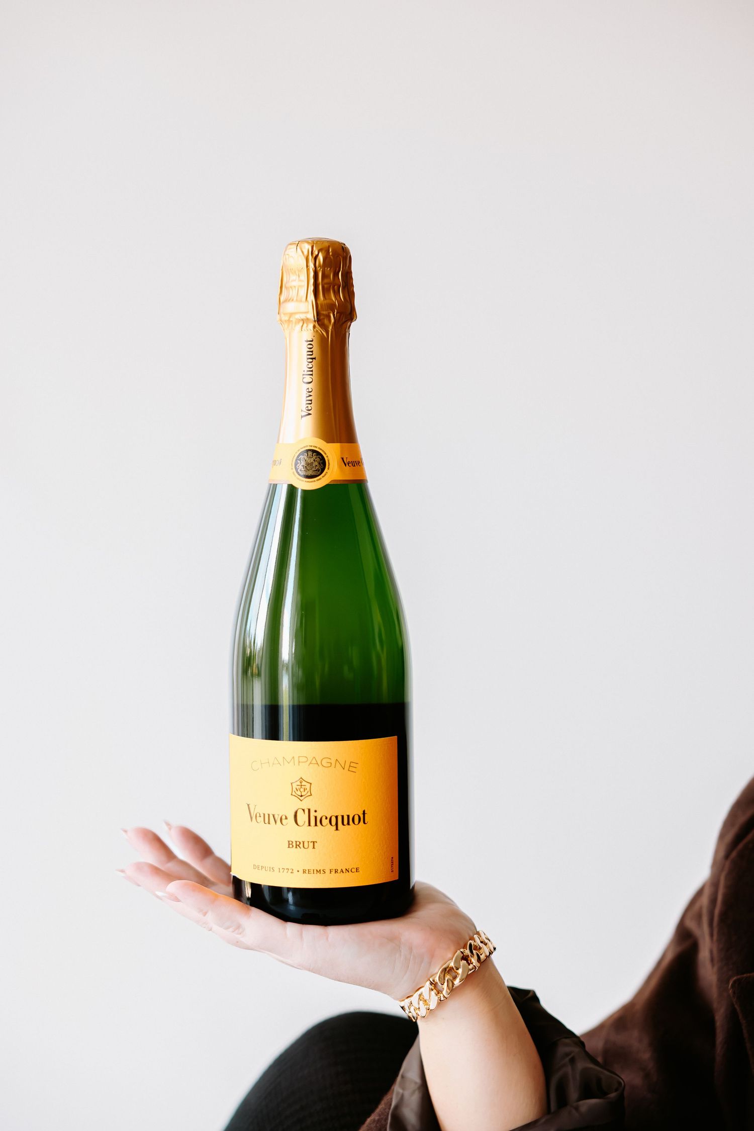 Hand holding a bottle of Veuve Clicquot Brut Champagne with iconic yellow label and gold foil top.