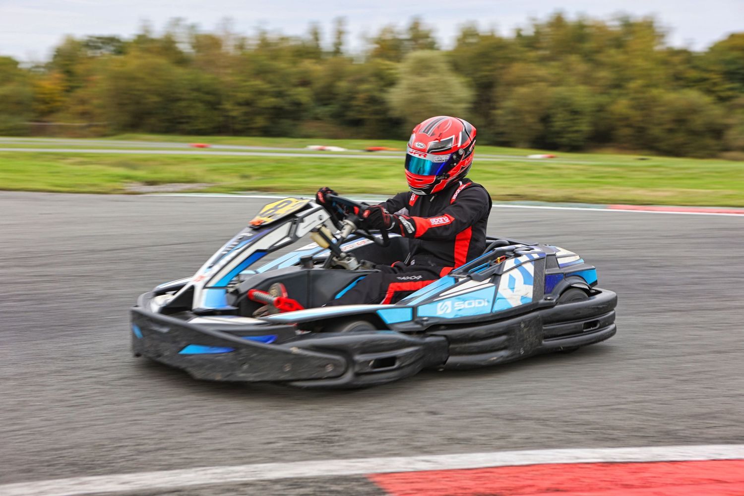 Go-kart racer in red and black racing suit navigating a corner on the track.