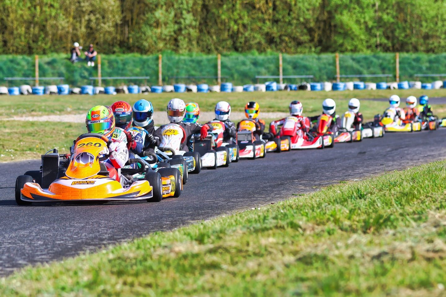 Colorful go-karts lined up on a racing track with grass and trees in the background.