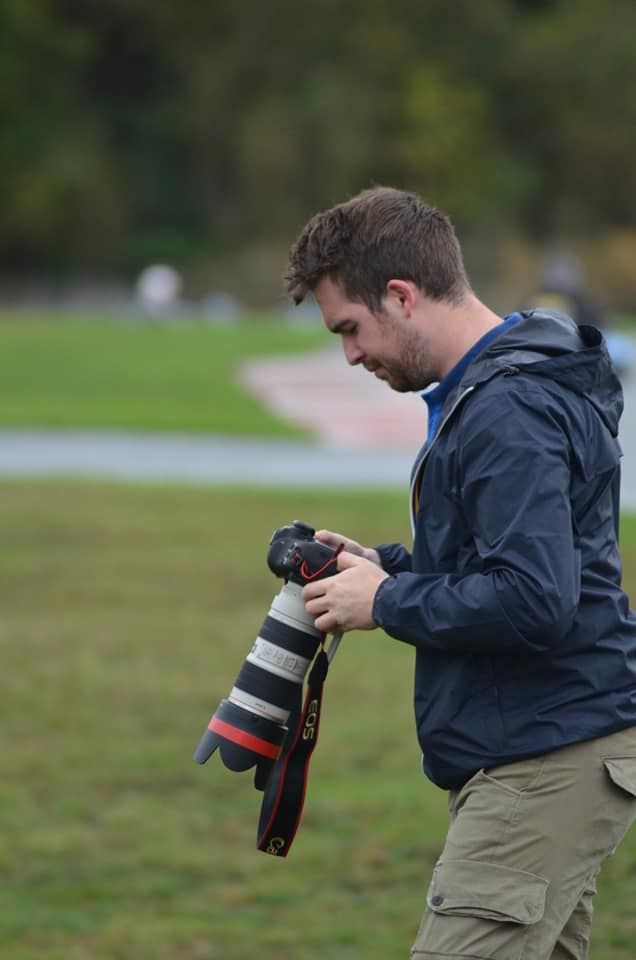 Photographer in navy jacket and khaki pants taking photos outdoors.
