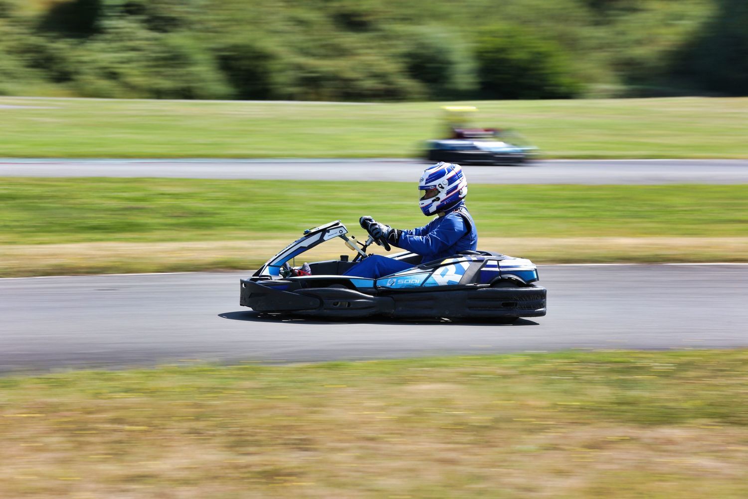 Go-kart racer in blue speeding around a track with motion blur effect.