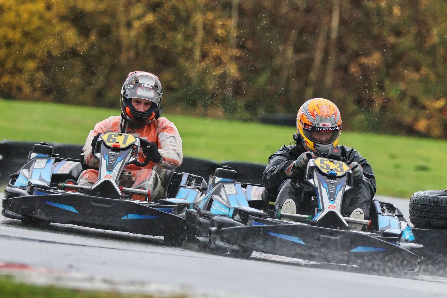 Go-karts racing around a track at high speeds with colorful helmets and suits.