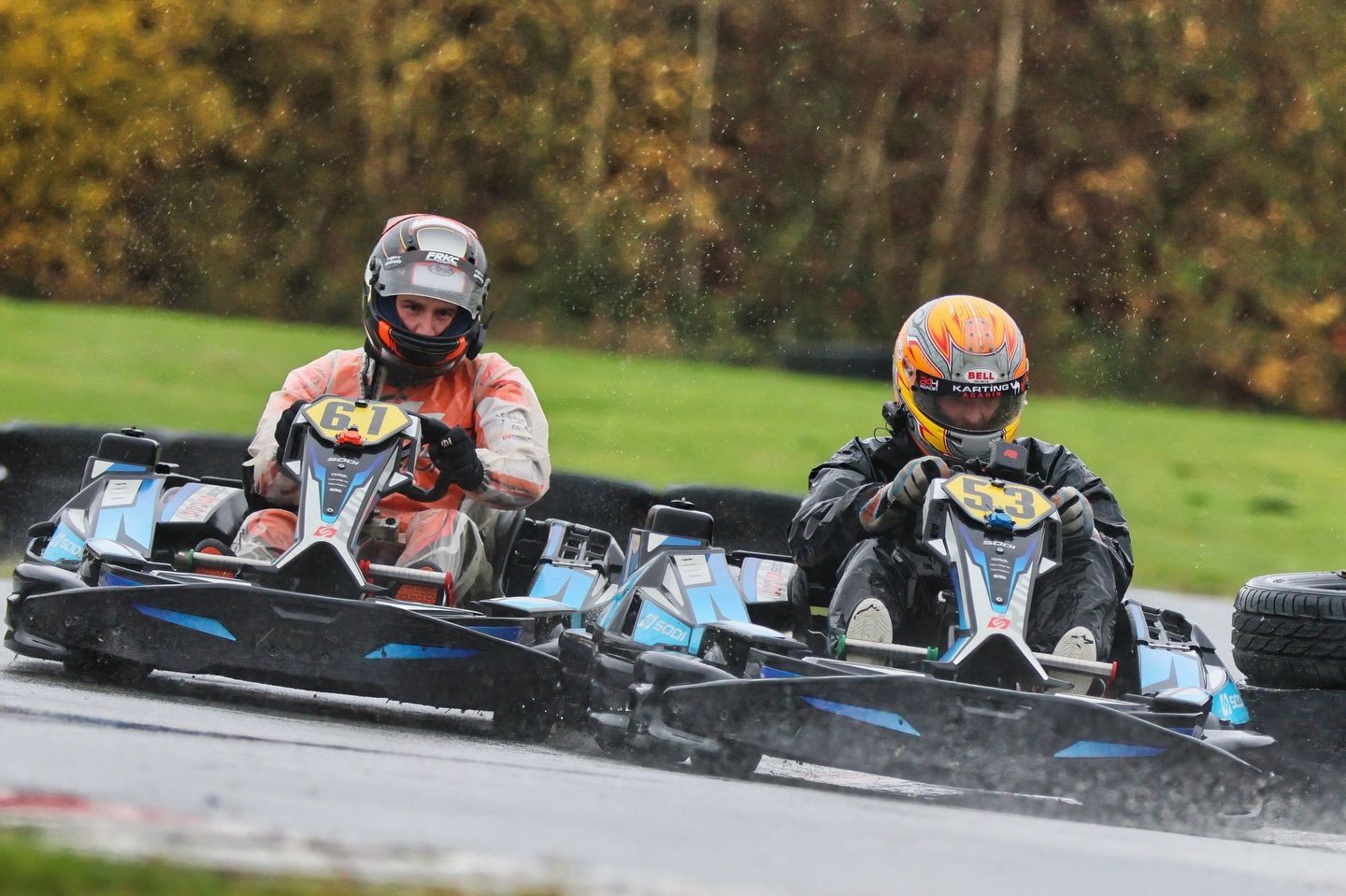 Multiple go-karts racing in formation through a curve on an autumn race day.
