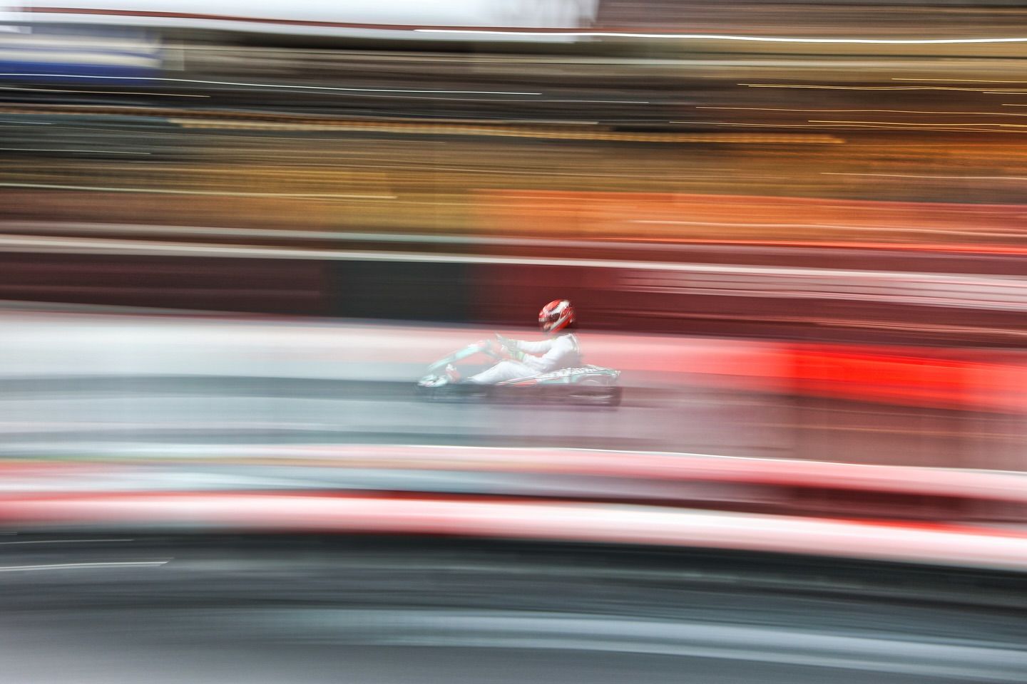 Motion blur effect of racing karts speeding past on a track with streaks of red and white light trails.