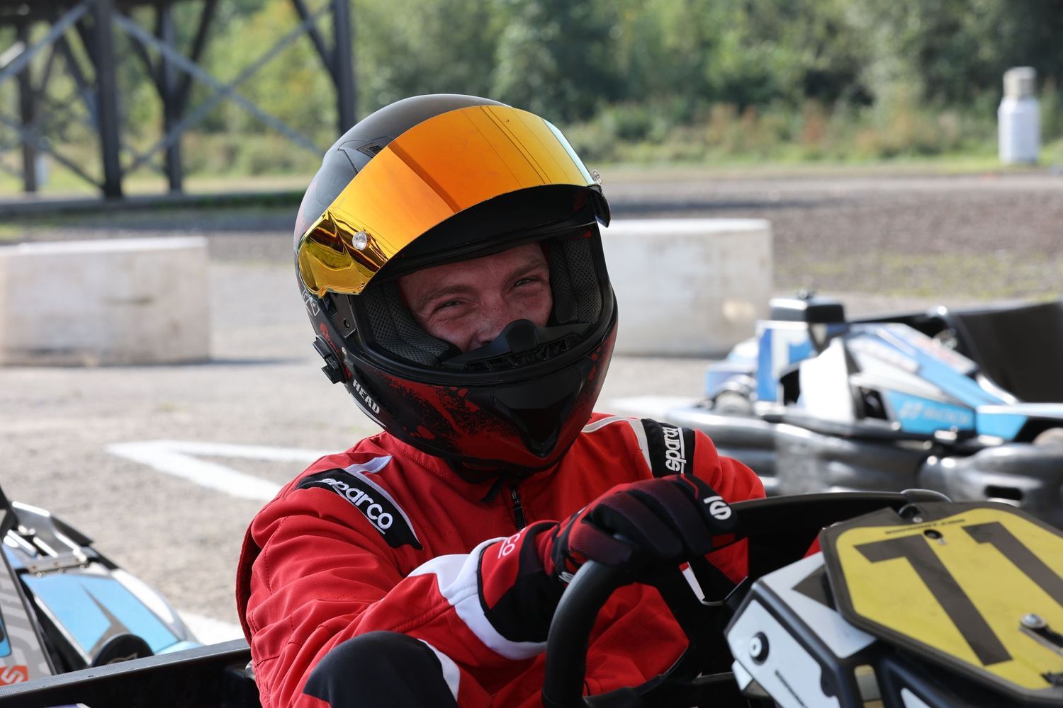 Racer wearing orange helmet in a go-kart on an outdoor racing track.