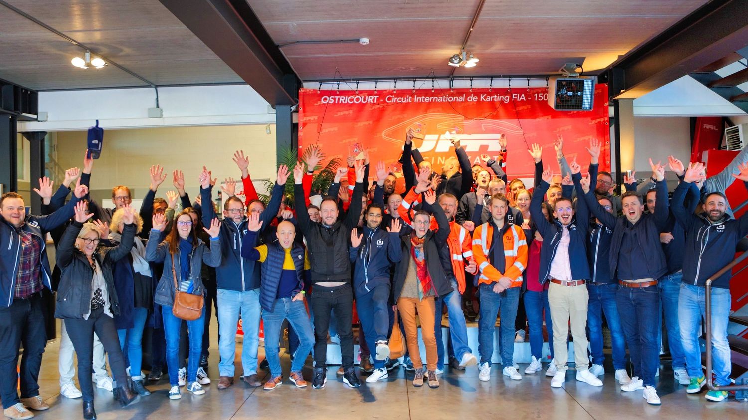 Large crowd of spectators lined up in a venue with orange lighting and industrial ceiling.